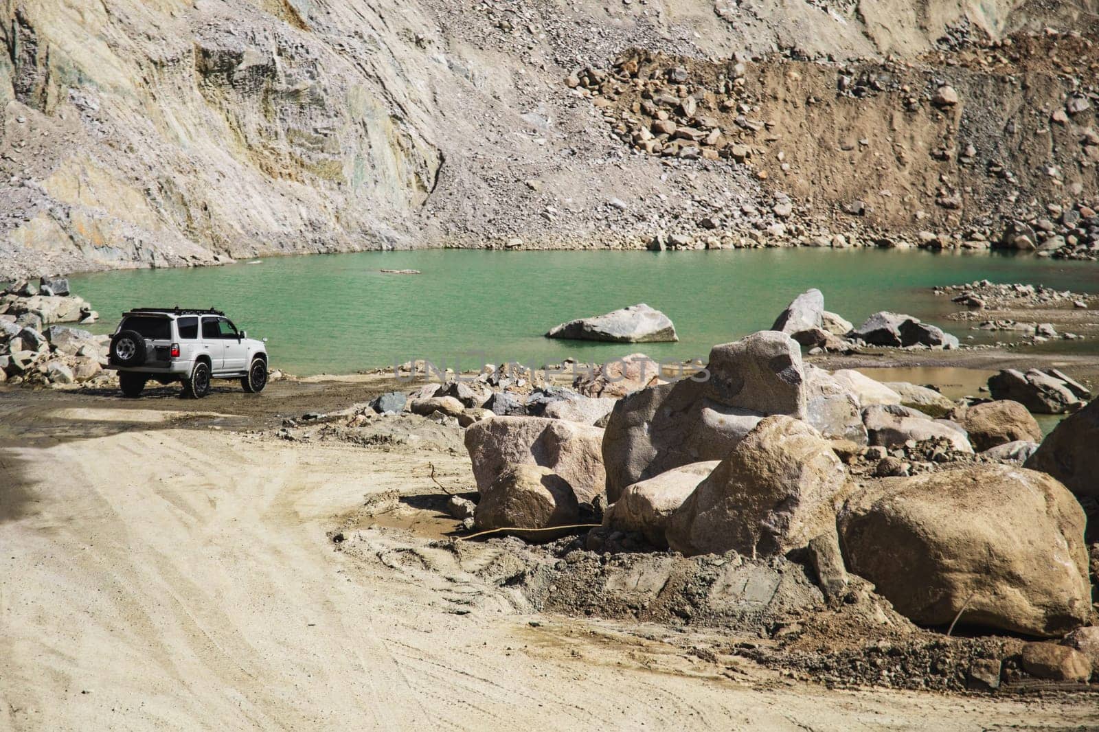 White off-road car in travel through mountains lake surrounded by rocky terrain.
