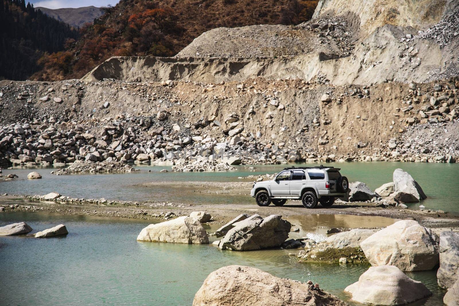 White offroader car in adventure of rocky mountains through river and lake.