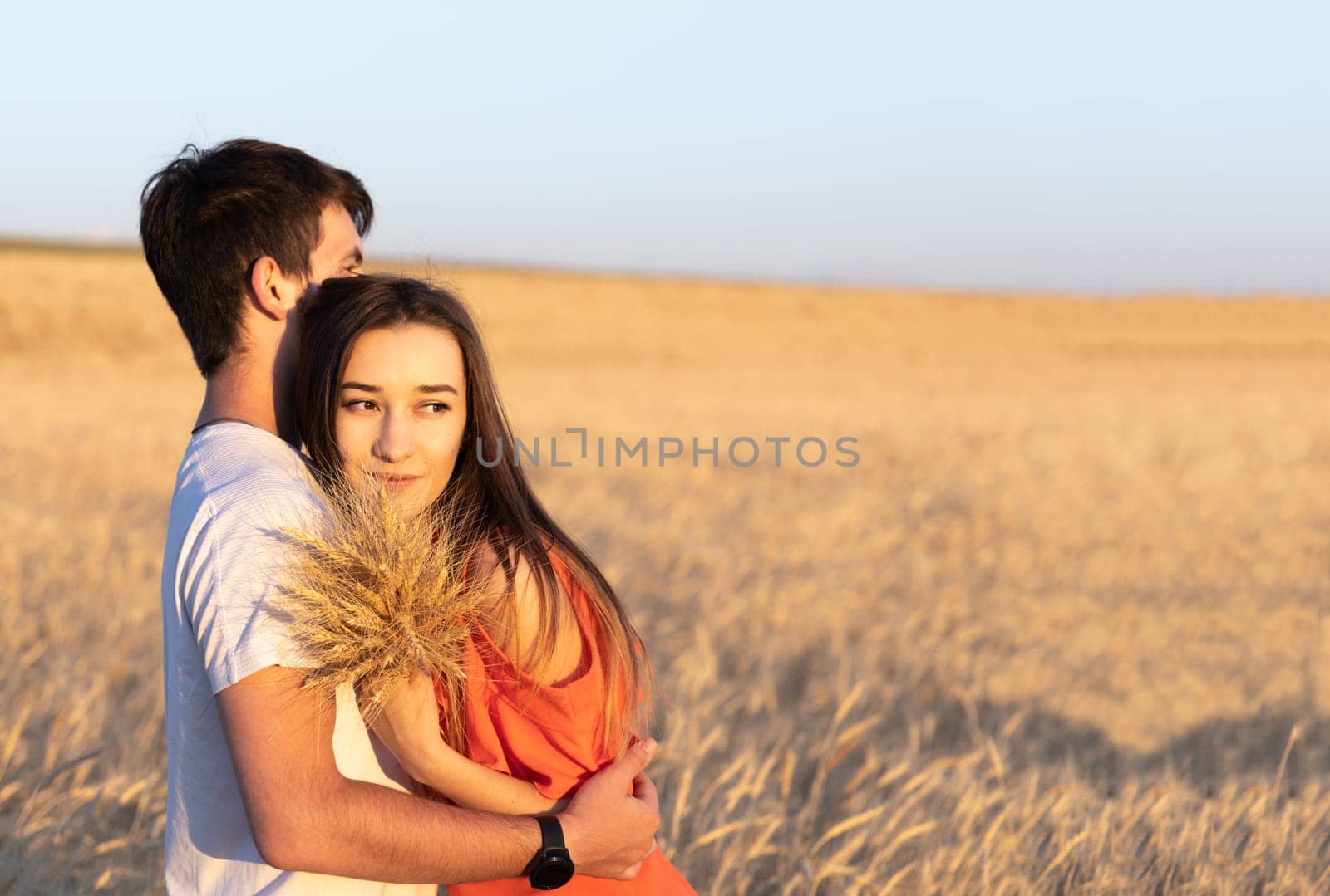 Young man hugging his girlfriend on sunset in wheat field. Copy space, love, togetherness concept. by Ri6ka