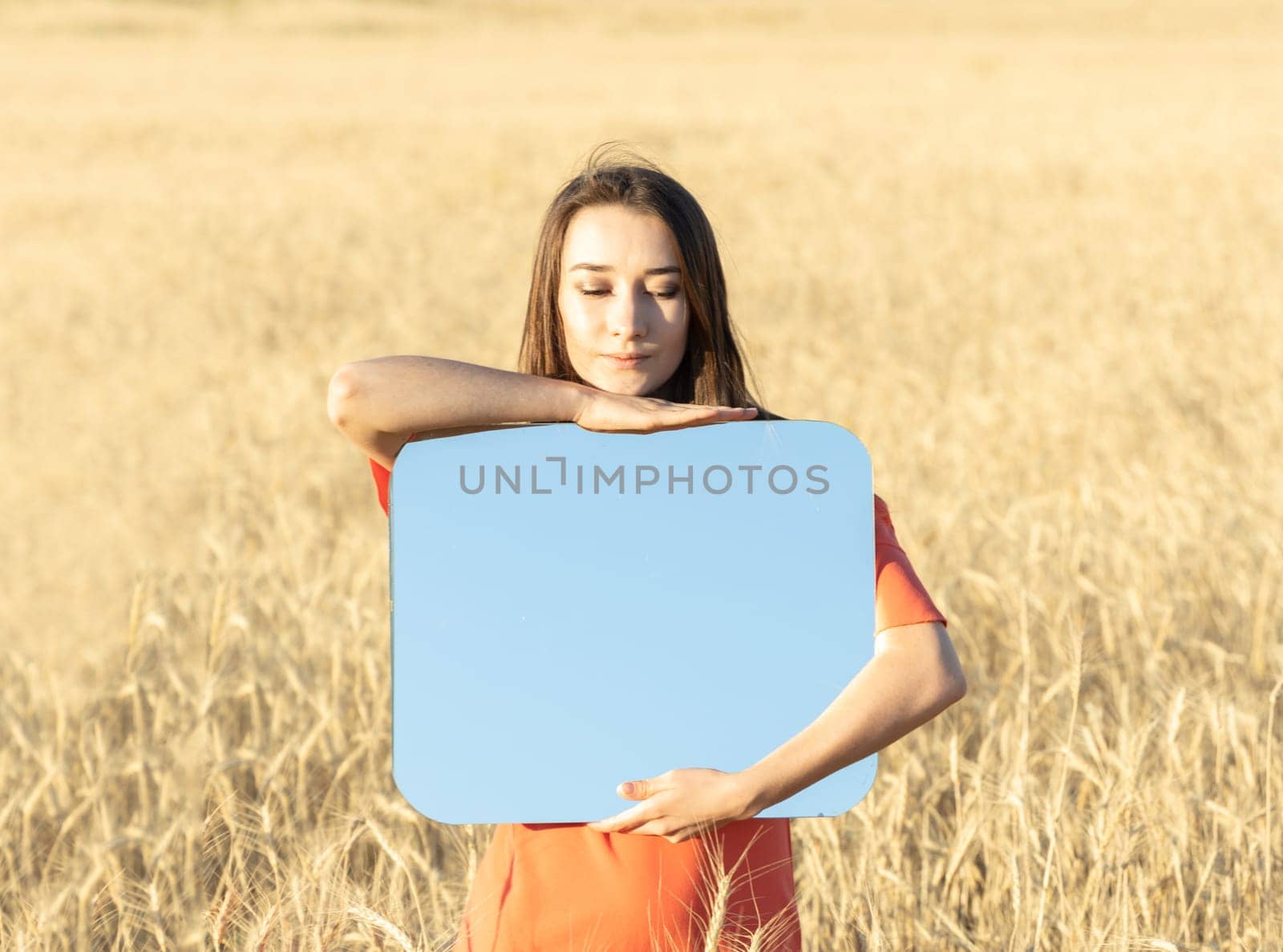 Young woman in the wheat field, holding mirror glass where reflected the blue sky. Meditation, mental health concept. Copy space