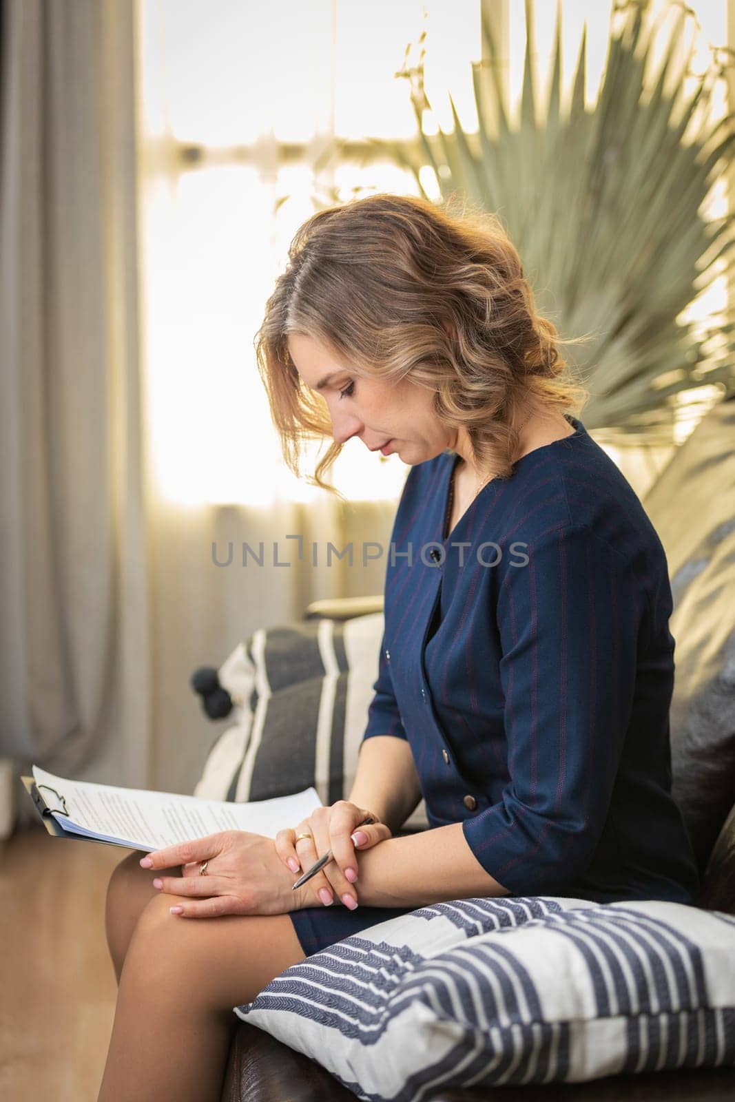 Portrait of a successful female psychologist in her office, notebook in hand, on the couch. Side view