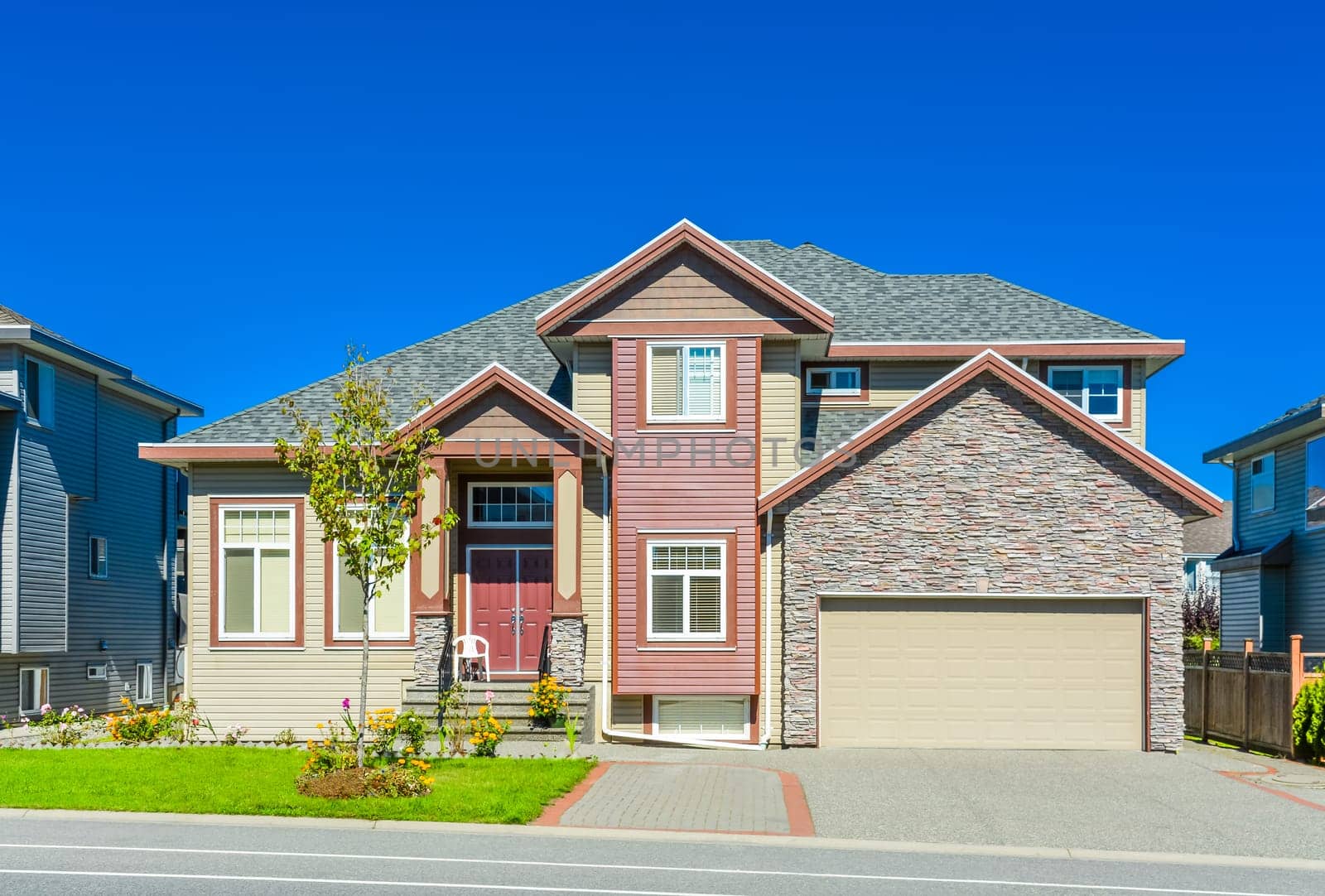 New family house on sunny day with landscaped lawn in front and blue sky background. New house with concrete driveway and asphalt road in front.