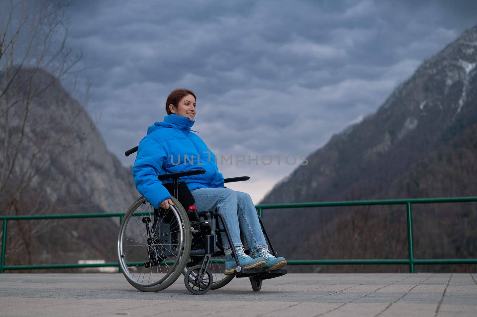 A woman in a wheelchair on a point view admires the high mountains. Thrust to life