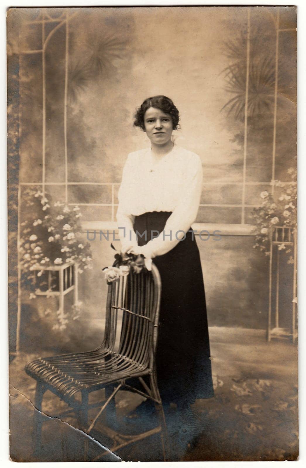 Vintage photo shows young woman poses with flowers in a photo studio. Photography with sepia effect. by roman_nerud