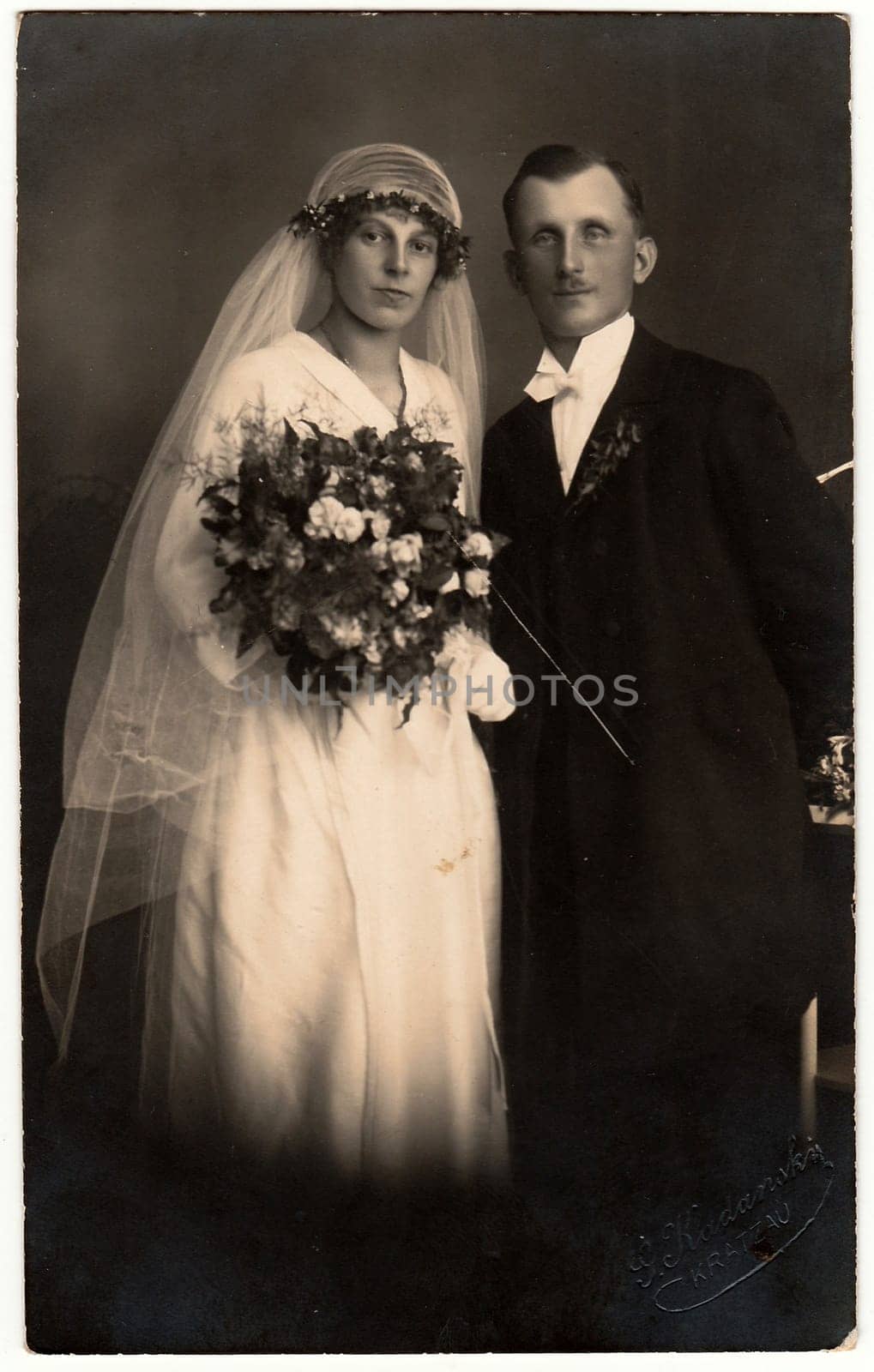 CHRASTAVA KRATZAU , THE CZECHOSLOVAK REPUBLIC - CIRCA 1930s: Vintage photo of newlyweds. Bride wears a long veil and holds wedding bouquet. Groom wears black suit and white bow tie. Black white antique studio portrait.