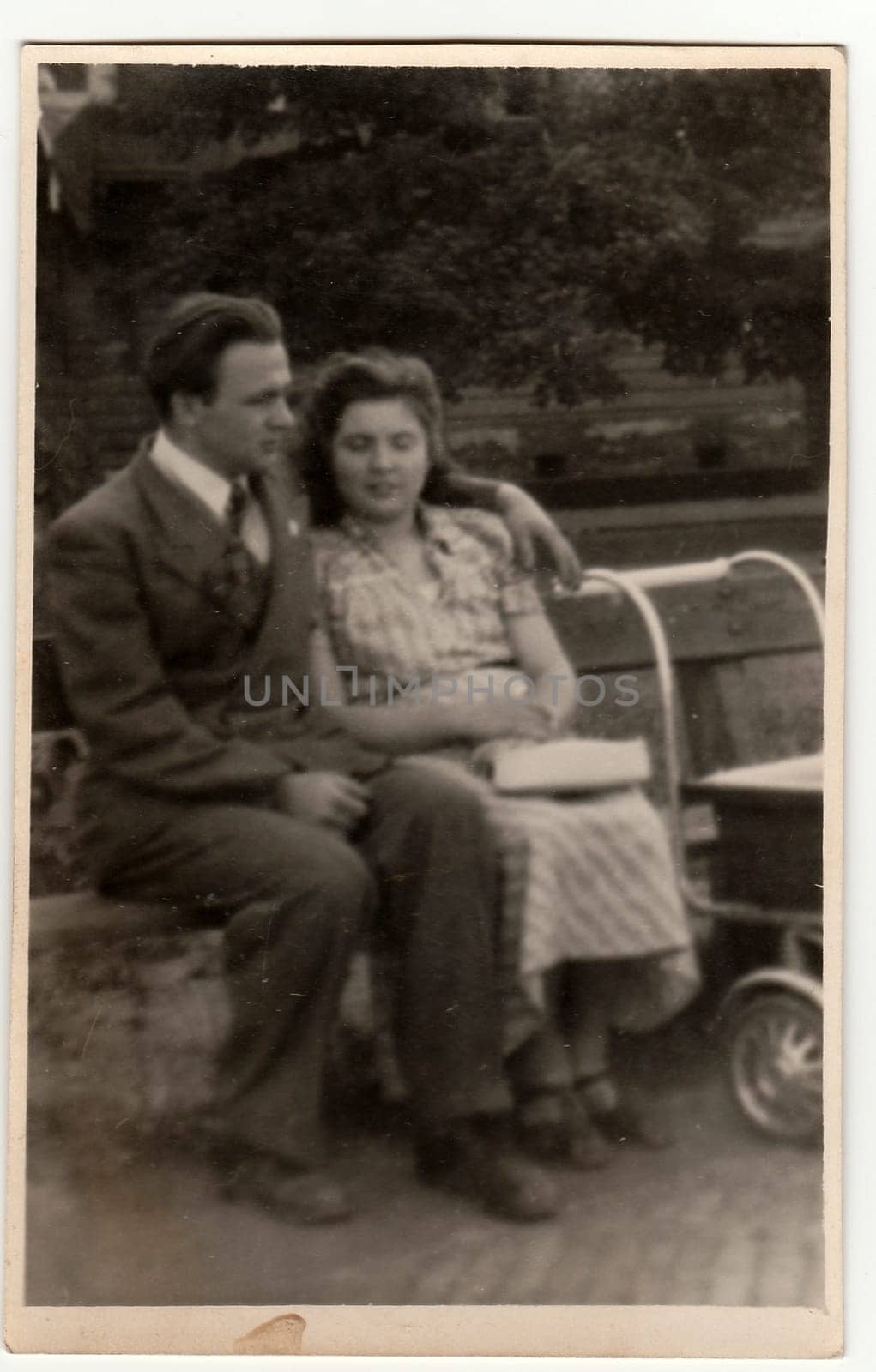 ITALY - CIRCA 1940s: Vintage photo shows a young couple with pram. Couple sits on a bench in the city park. Black & white antique phtography.