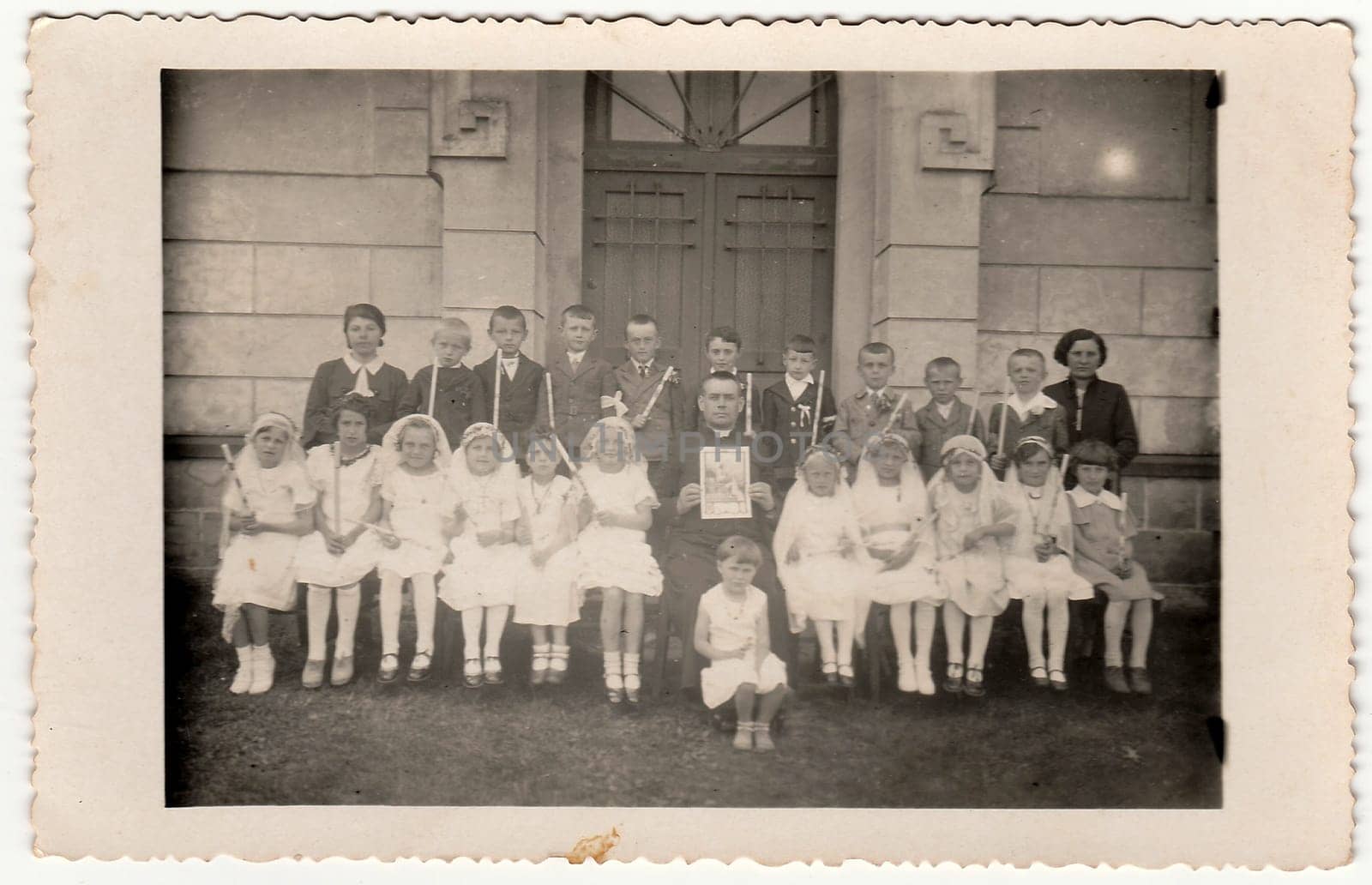 Vintage photo of children at the First Communion. On photography is a priest and female teacher schoolmistress . by roman_nerud