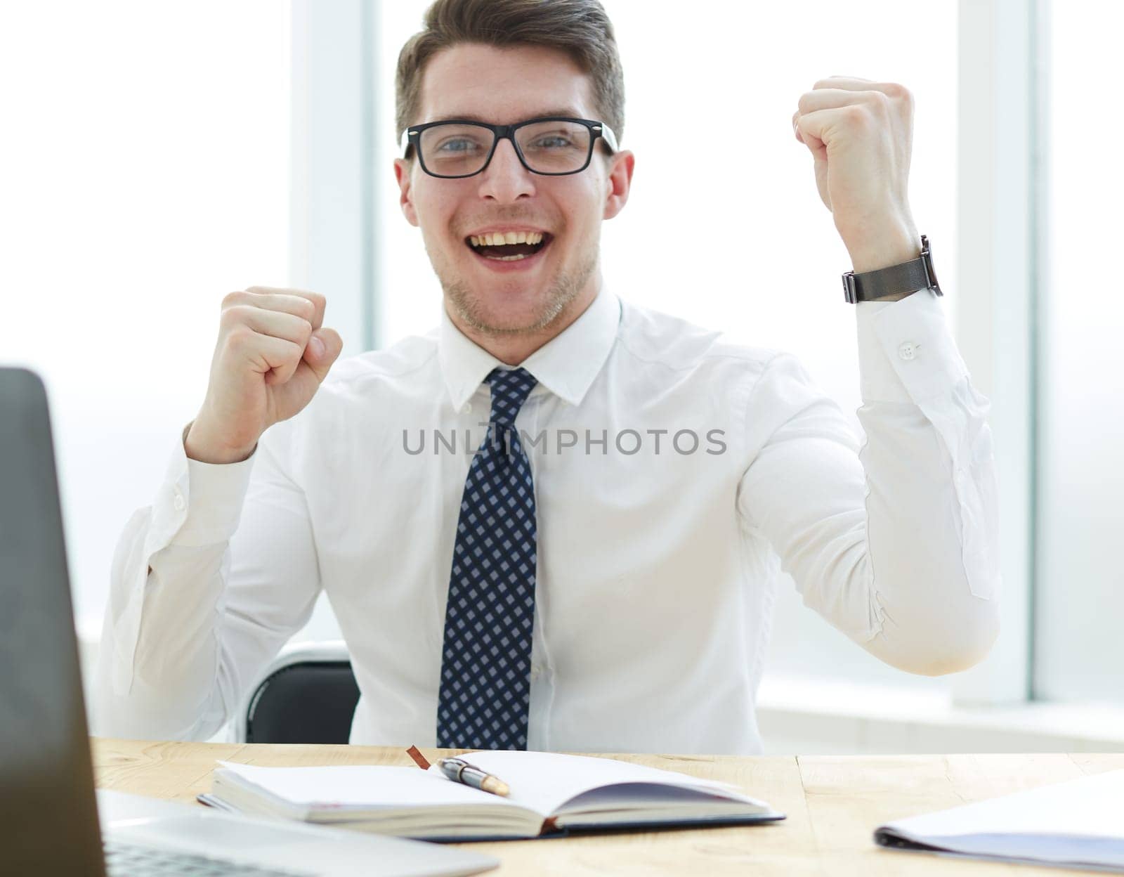 Happy young businessman raising hands in front of laptop