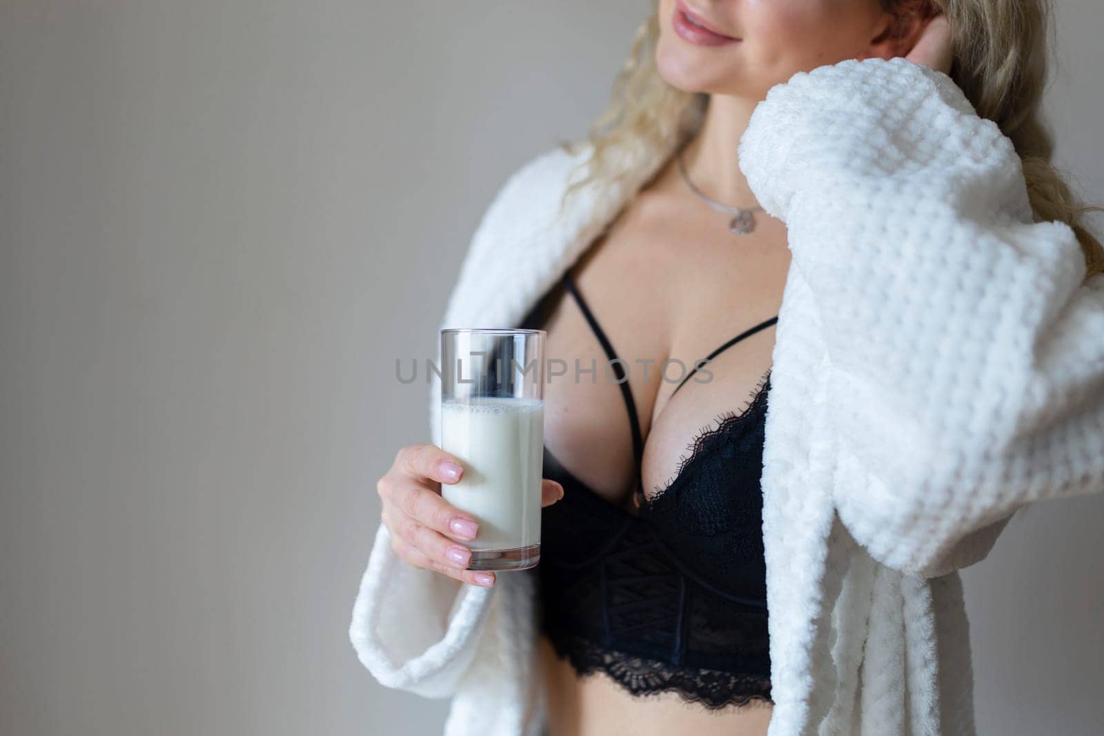 sexy young woman in black lingerie pouring milk on body isolated on grey.