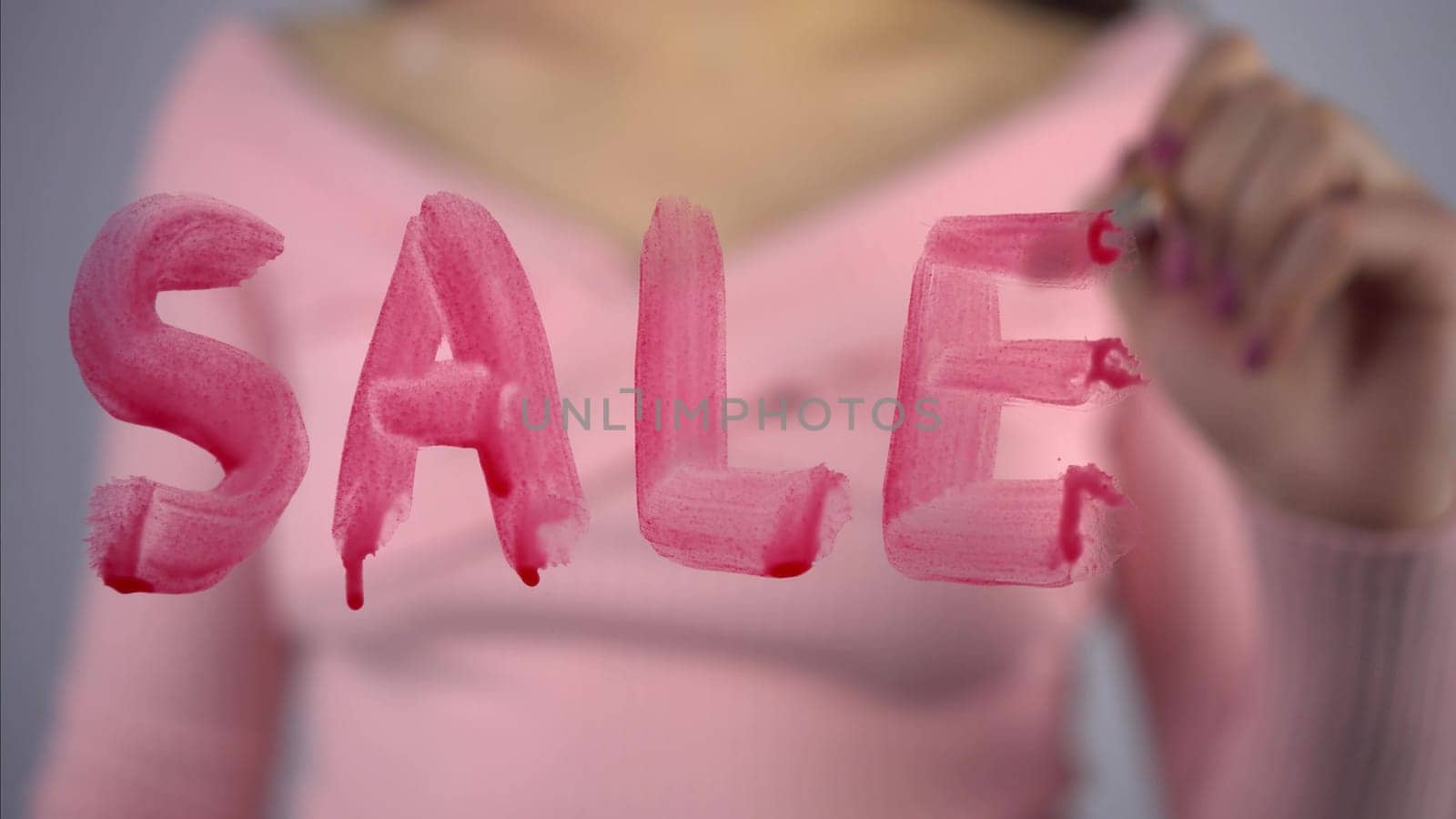 A young woman draws the word sale on the glass. A girl in a pink sweater draws with a brush and red paint. Close-up. 4k