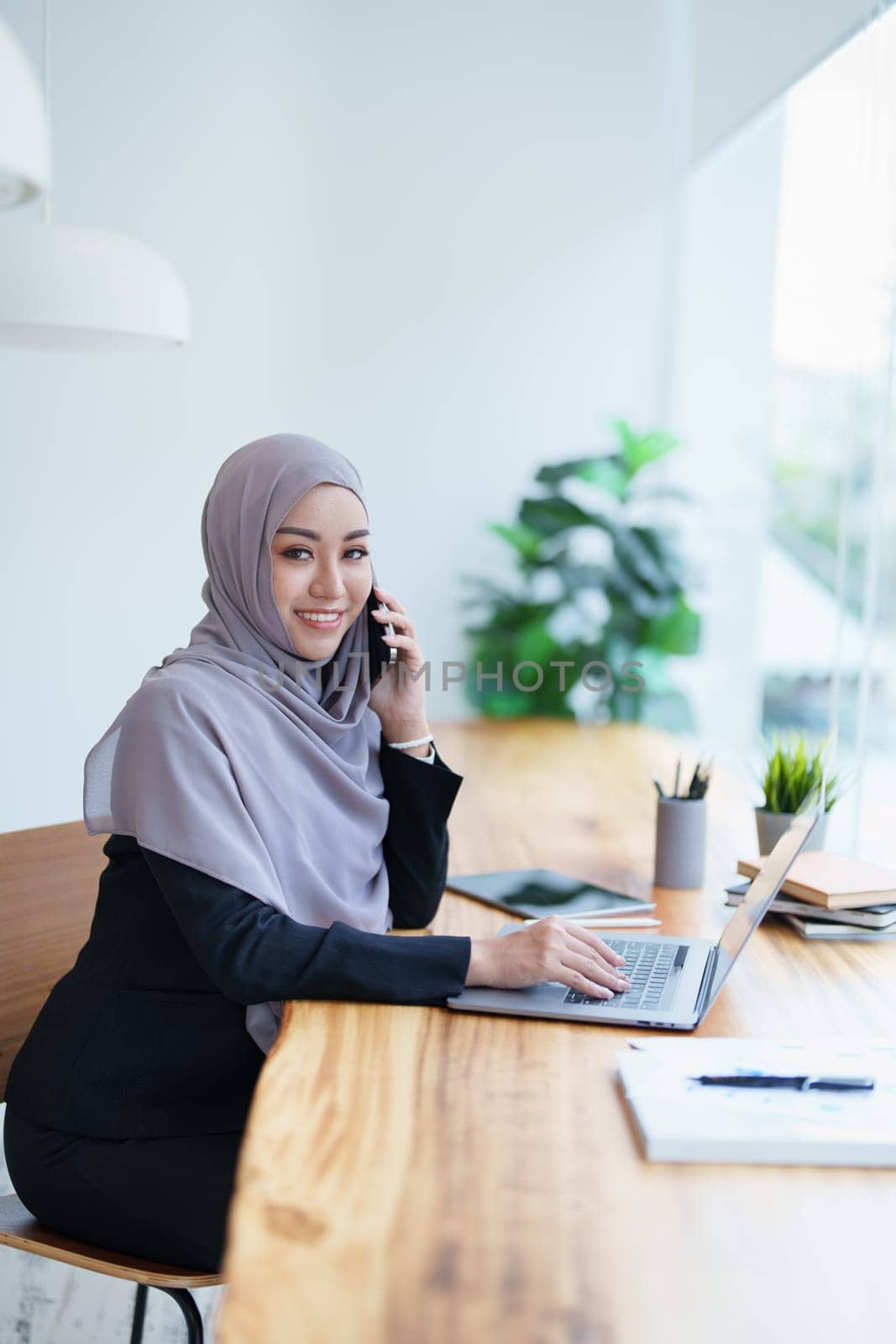 Beautiful Muslim woman talking on the phone and using a computer on her desk by Manastrong