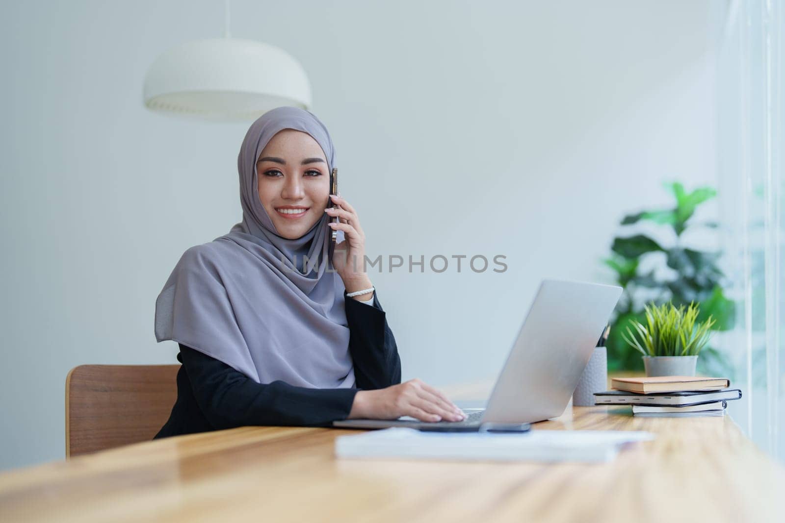 Beautiful Muslim woman talking on the phone and using a computer on her desk.
