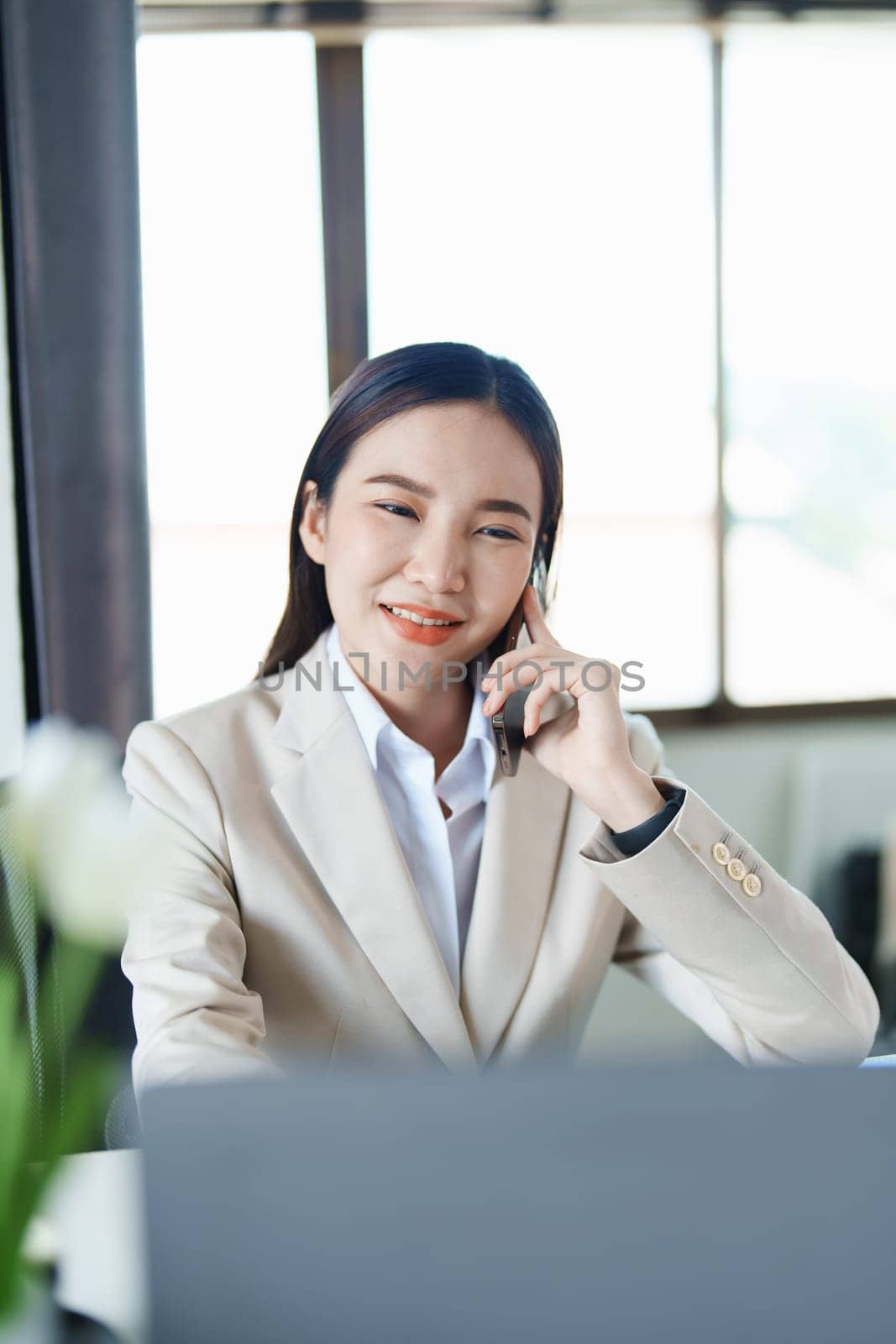 Portrait of a young Asian woman showing a smiling face as she uses her phone, computer and financial documents on her desk in the early morning hours by Manastrong