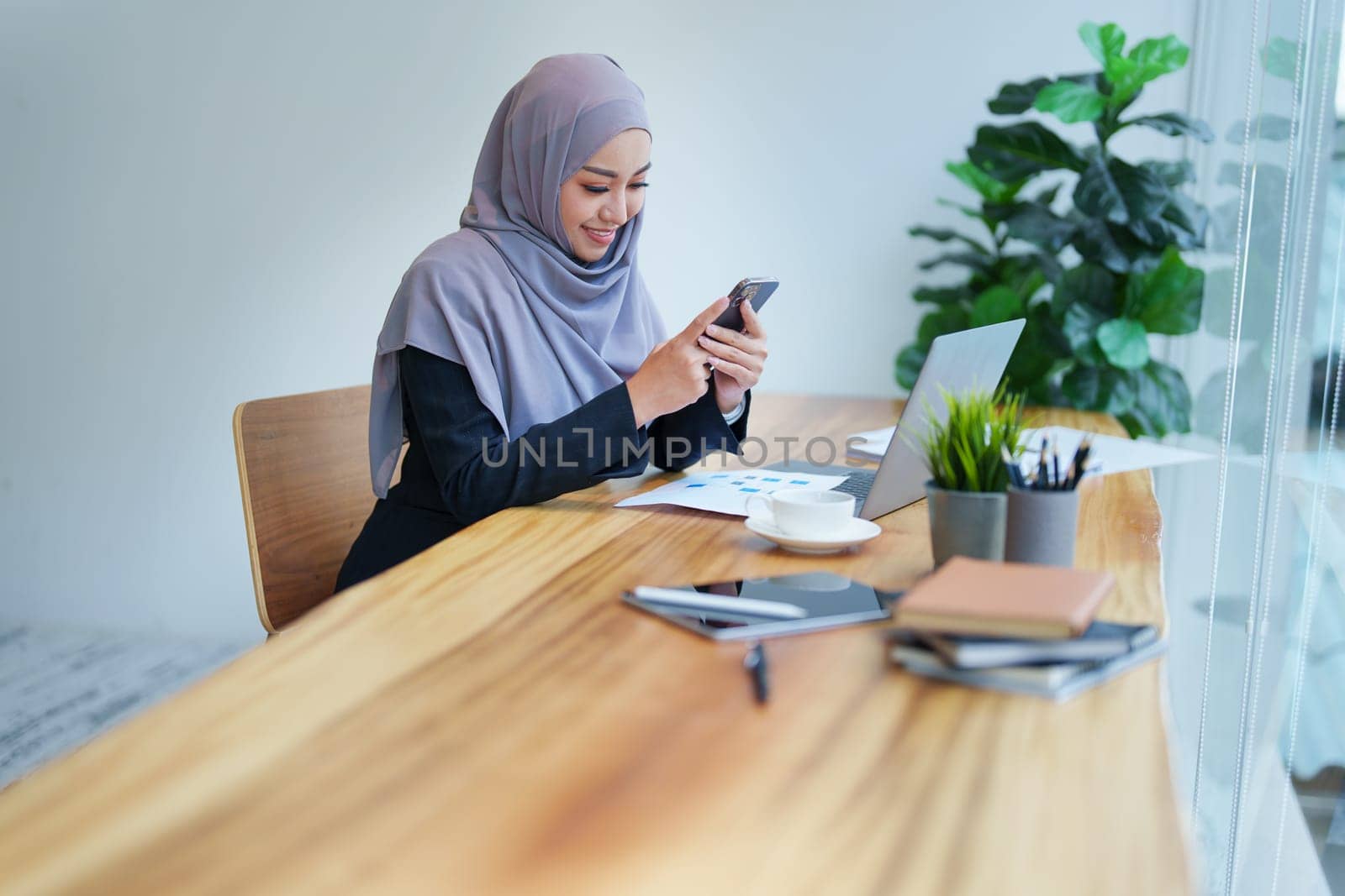 Beautiful Muslim woma talking on the phone and using a computer on her desk by Manastrong