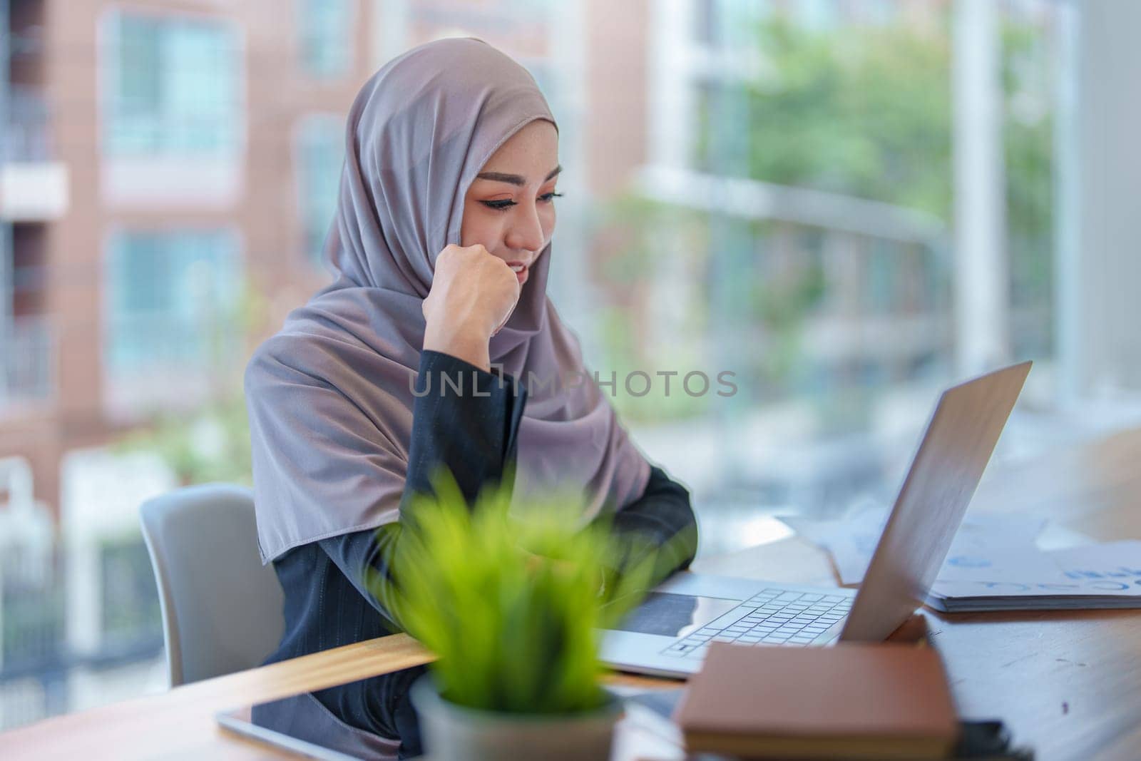 A beautiful Muslim woman showing a smiling face in the morning using computers and documents working at the office.