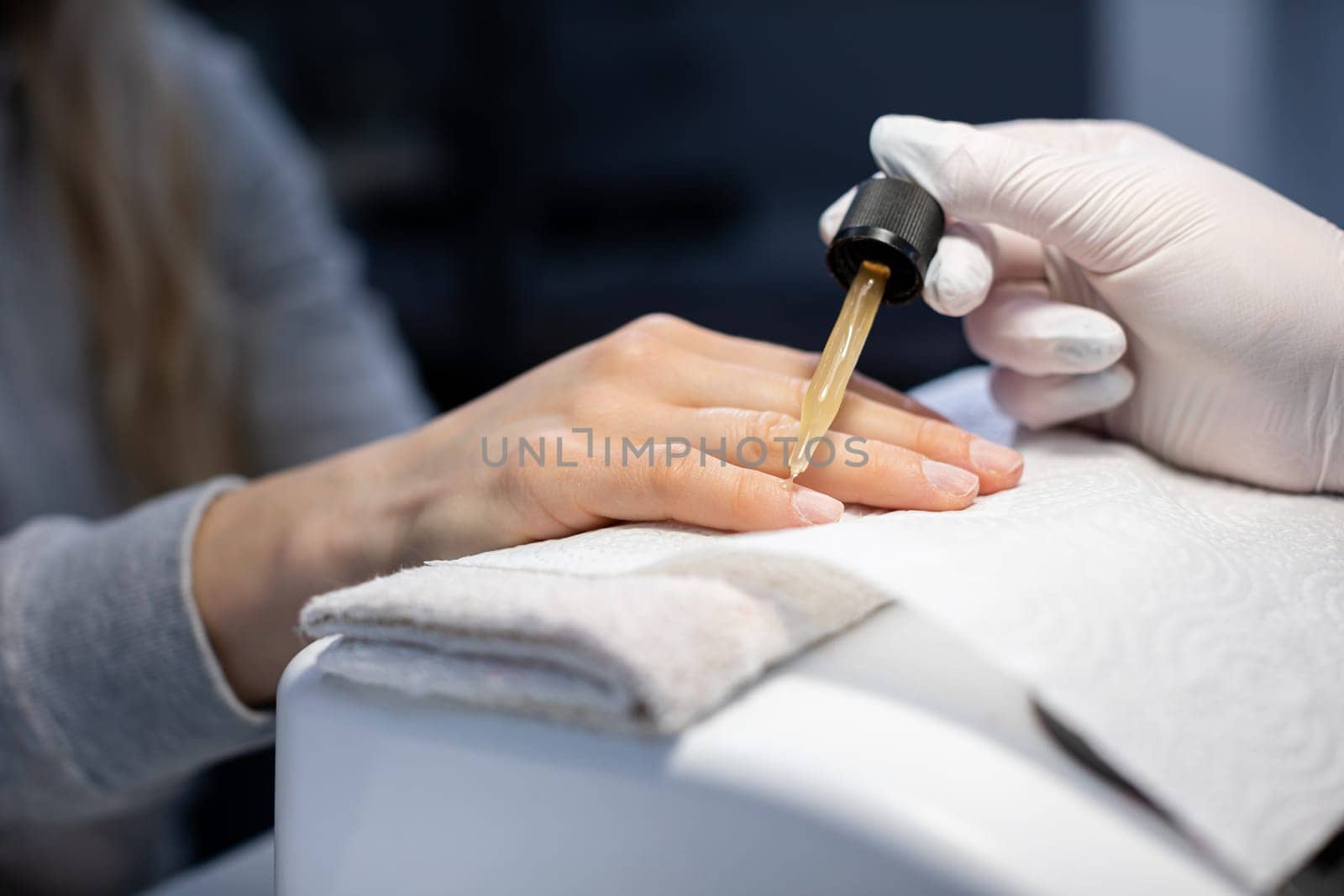 The beautician wears disposable nitrile gloves. Maintaining the rules of hygiene in the beauty salon. The professional nourishes the client's nails with cosmetic oil.