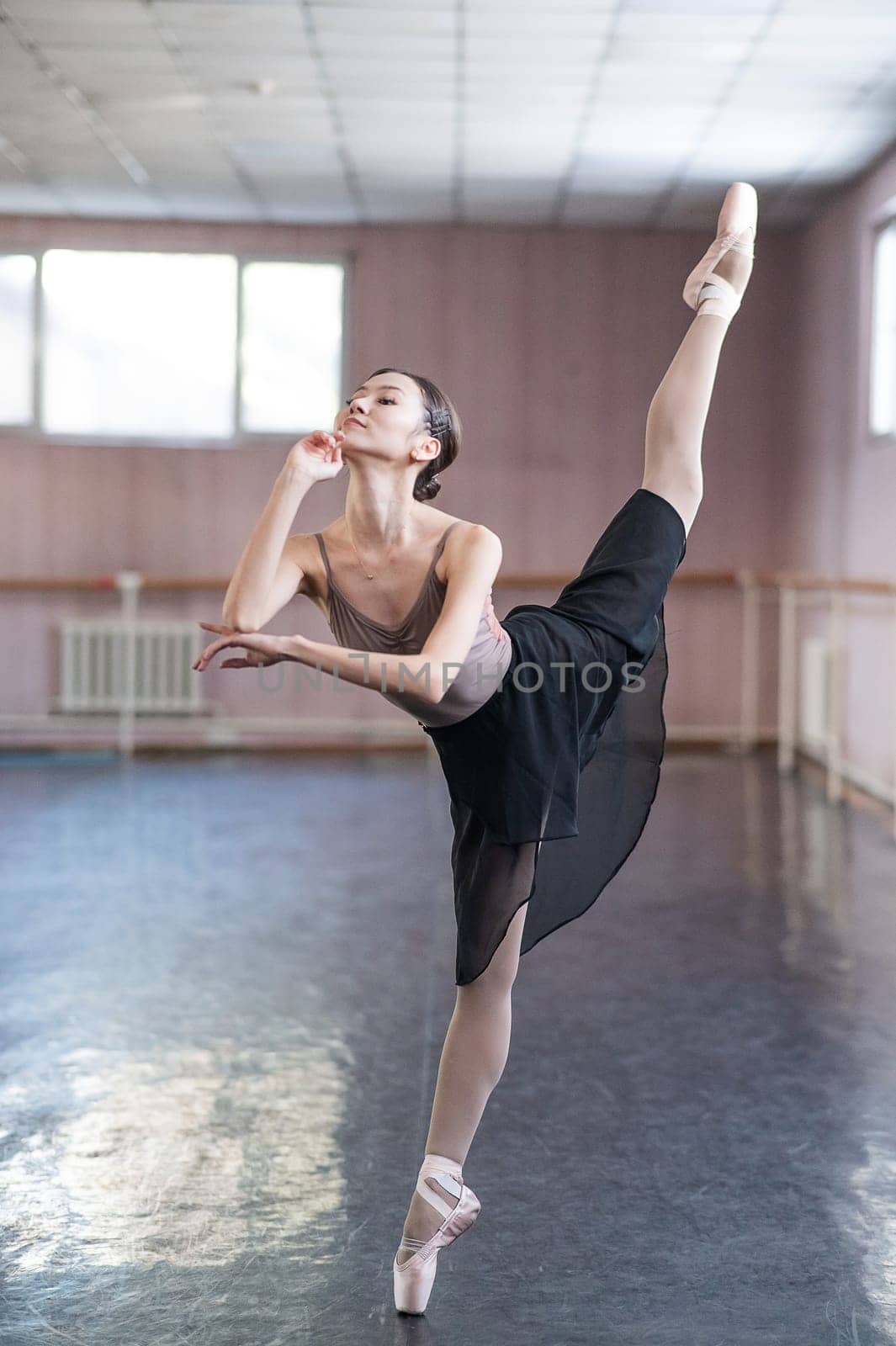 Graceful Asian ballerina in a beige bodysuit and black skirt is rehearsing in a dance class