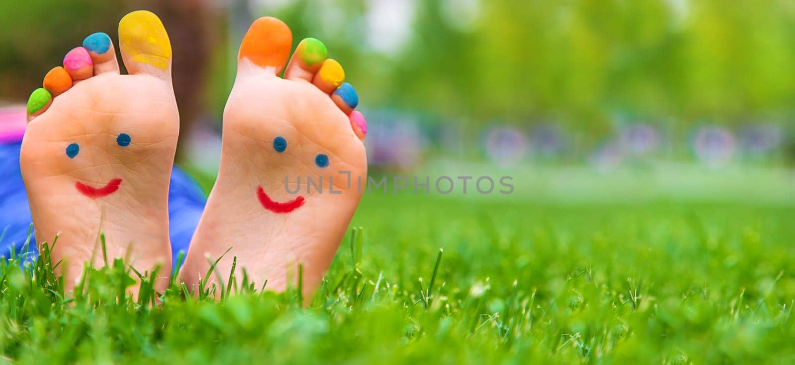 Feet of a child on the grass with a painted smile. Selection focus. by yanadjana