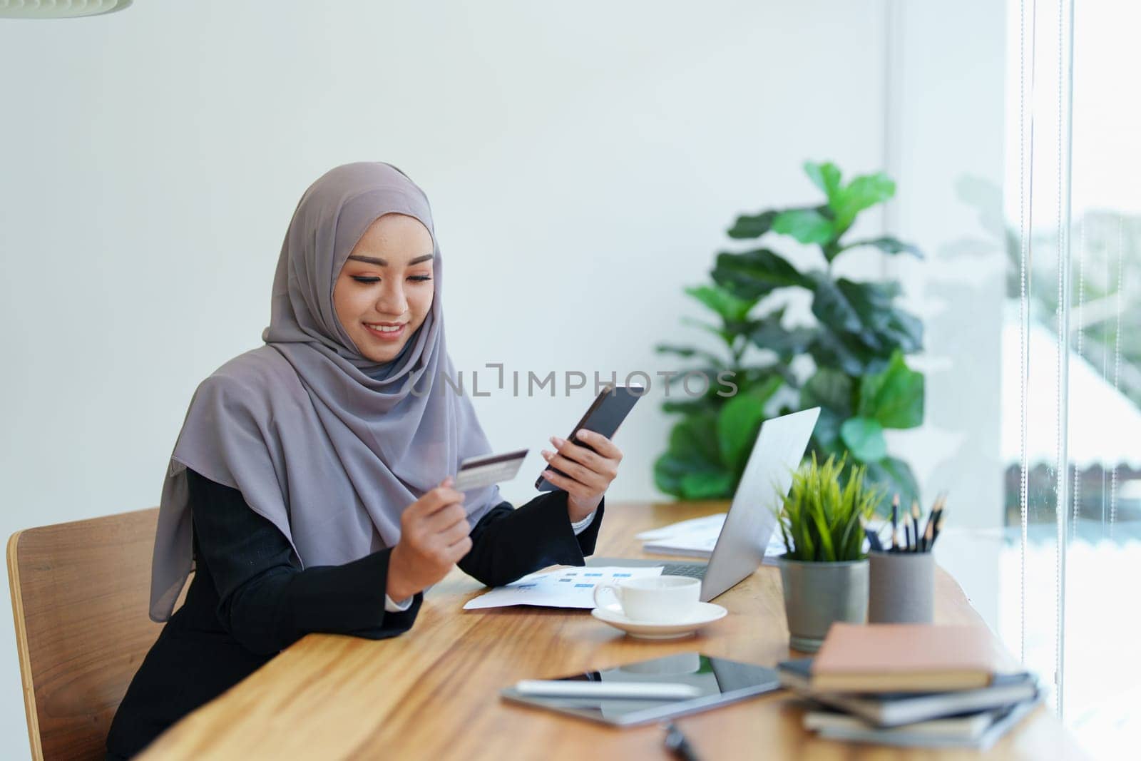 Beautiful Muslim woman shopping online using her phone and credit card by Manastrong