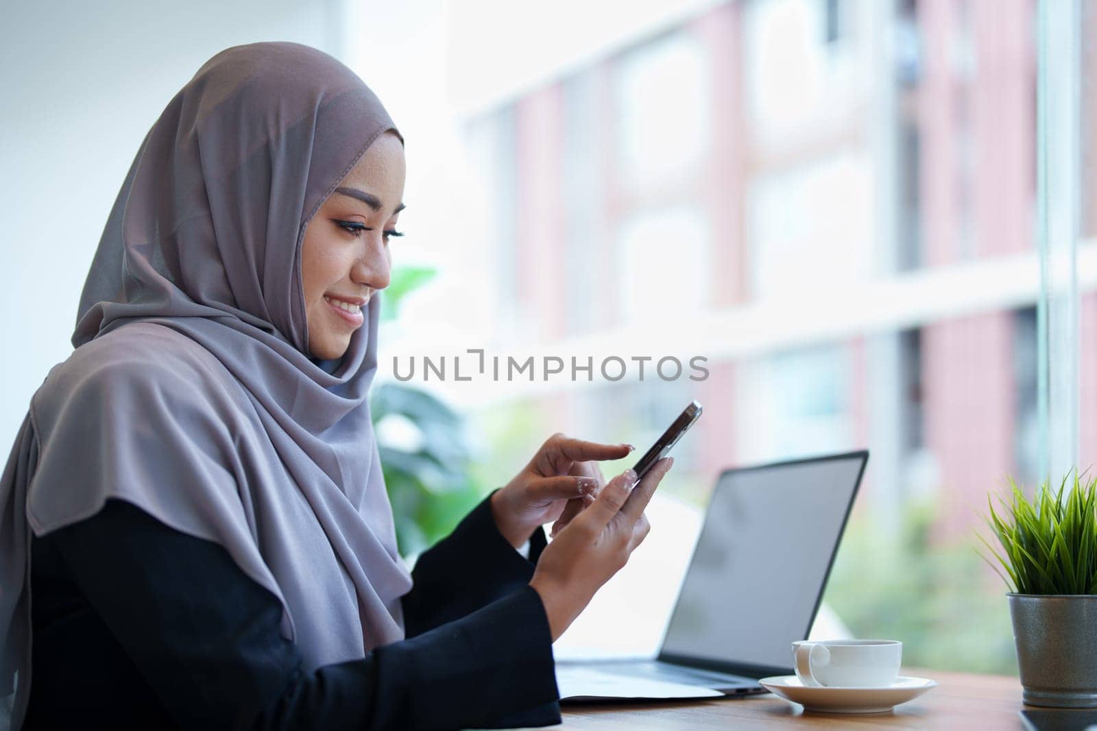 Beautiful Muslim woman talking on the phone and using a computer on her desk.
