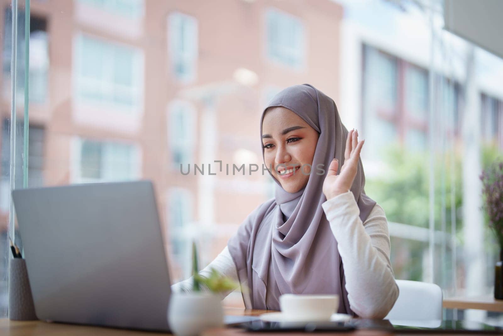 Beautiful Muslim woman using computer to greet attendees via video conference.