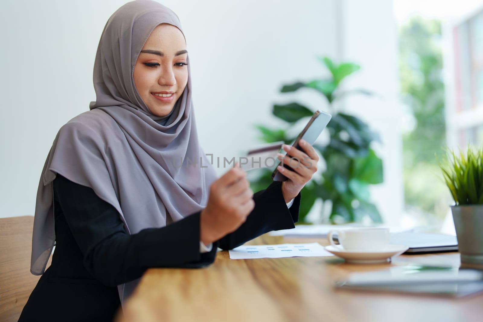 Beautiful Muslim woman shopping online using her phone and credit card.
