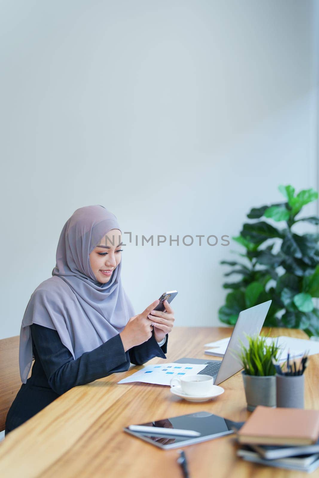 Beautiful Muslim woma talking on the phone and using a computer on her desk by Manastrong