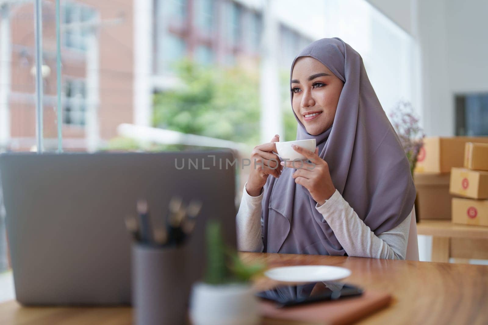 Beautiful Muslim woman using computer to check customer orders, small business owners or sme concepts.