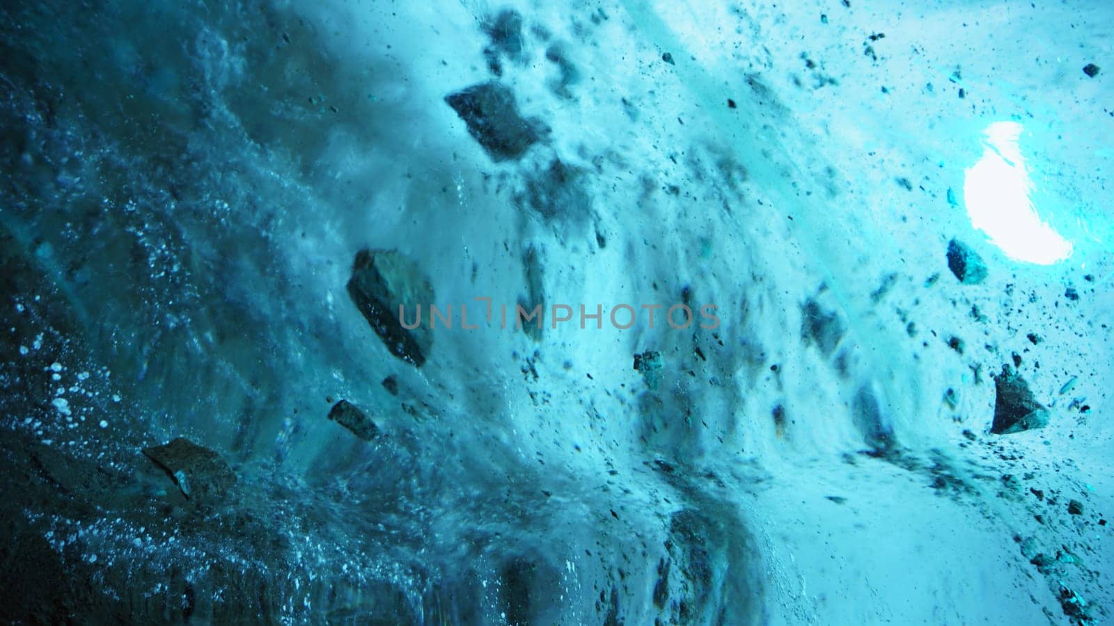 Turquoise pure color of ice inside the ice cave. Stones and icicles are visible in places. Light grains of snow on the ice walls. Frozen air bubbles in an ice wall. An ancient glacier. Color gradient