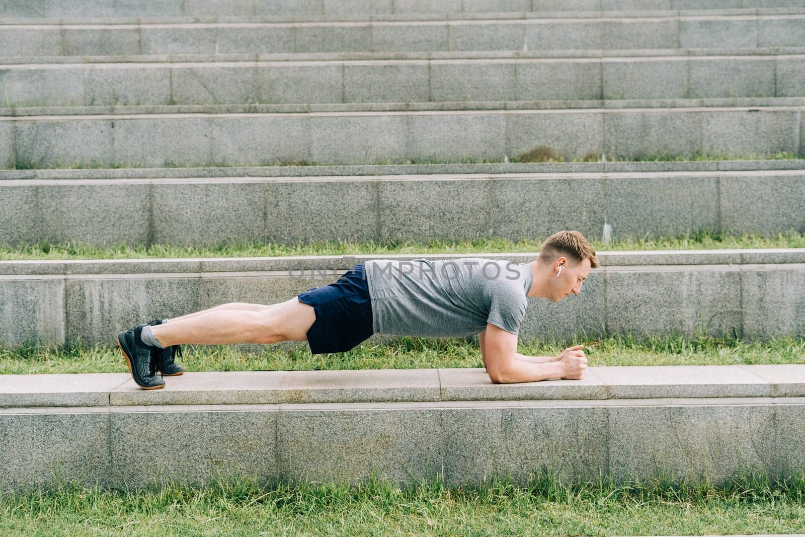 Young man has fitness workout. Male athlete does abs exercise, sport and training outdoor and stands in plank. People sport and healthy lifestyle concept.