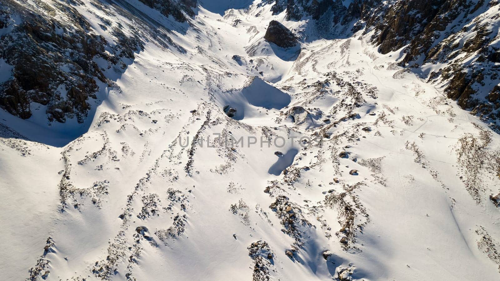 A huge frozen glacier in the mountains and a lot of tourists. Walking in the snow, taking photos with ice. Top view from a drone. Ice resembles marble. Dark light gray tones. Snowy mountains. Almaty