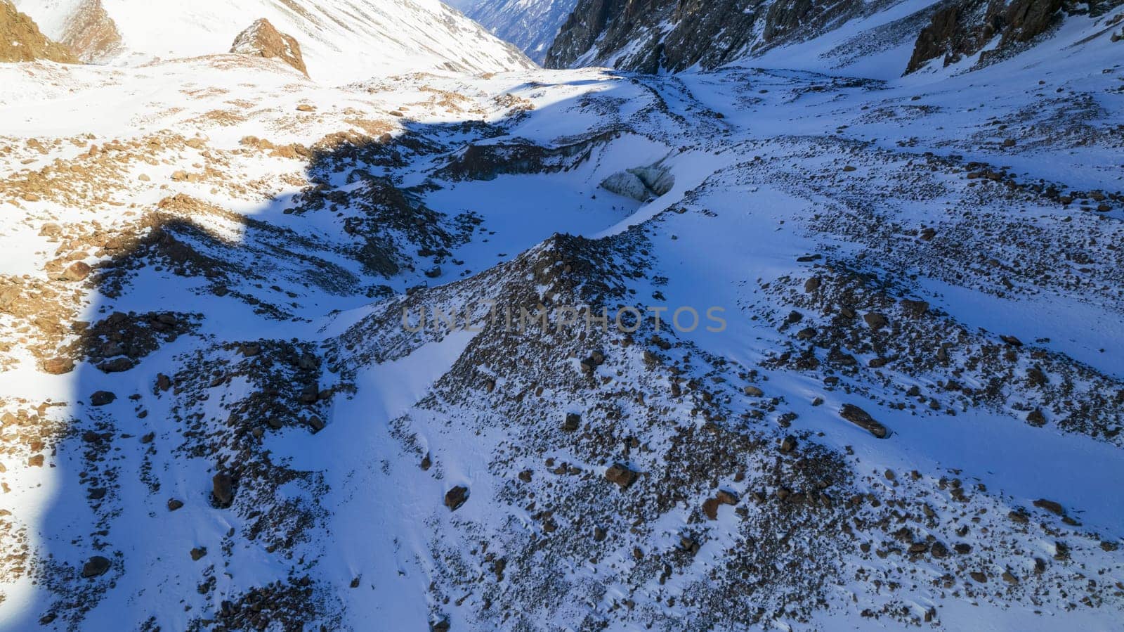 A huge frozen glacier in the mountains and a lot of tourists. Walking in the snow, taking photos with ice. Top view from a drone. Ice resembles marble. Dark light gray tones. Snowy mountains. Almaty