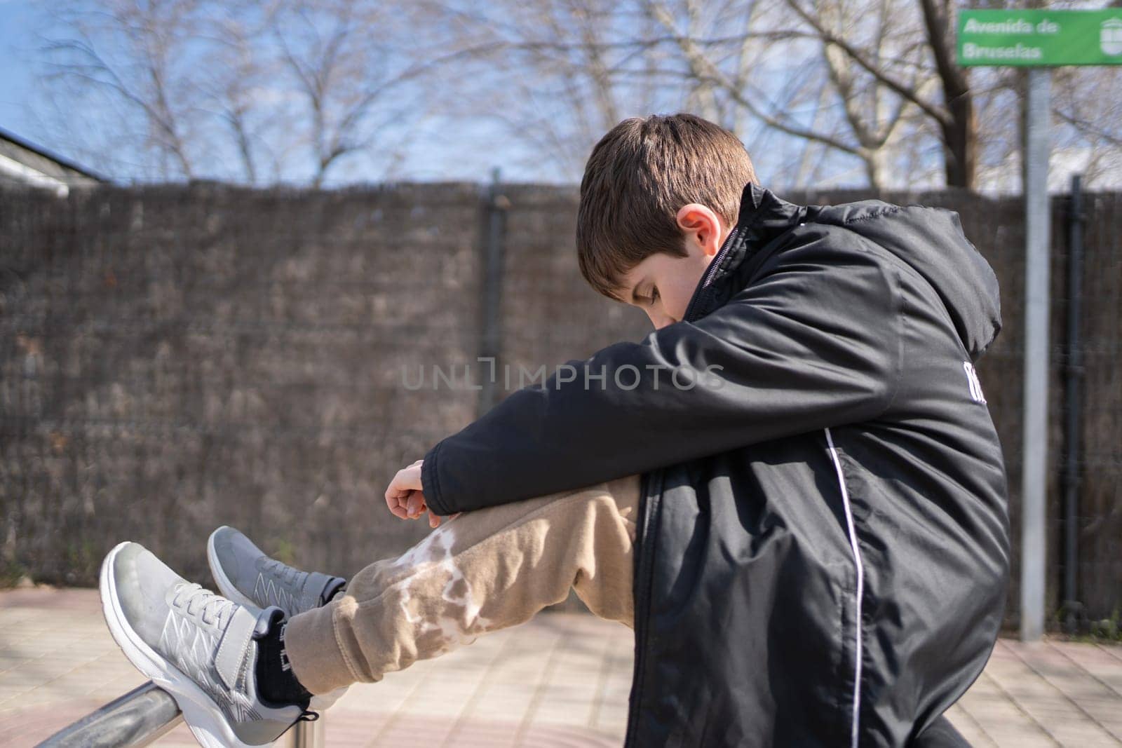 Side view of sad schoolkid sitting with his head down in the street. High quality photo