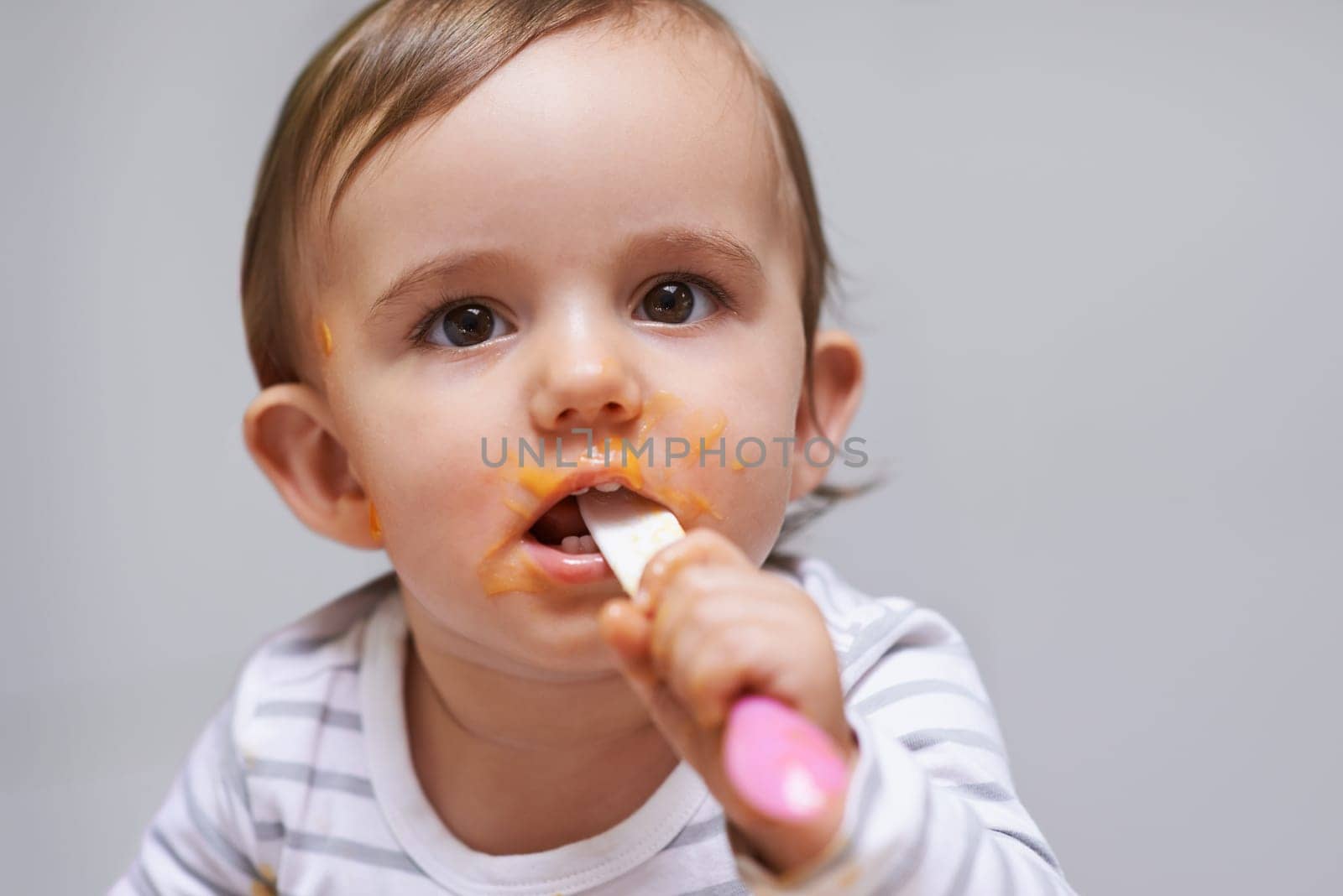 Messy and adorable. a cute little baby girl eating with a spoon. by YuriArcurs