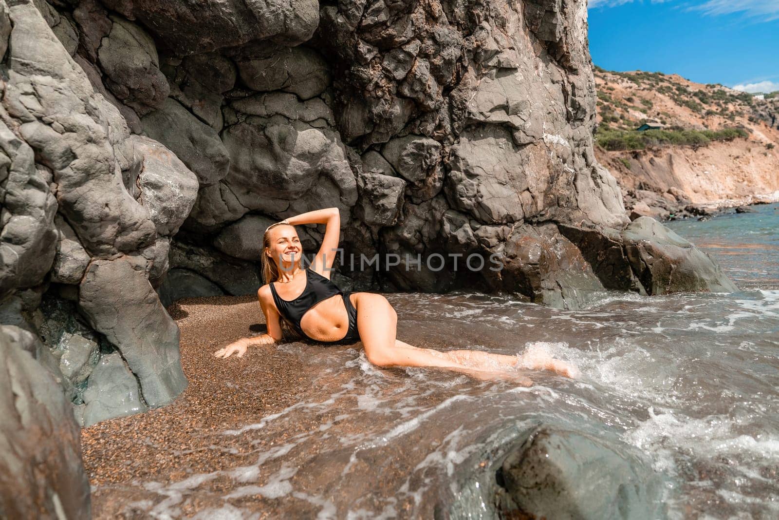 Woman swimsuit sea. Attractive blonde woman in a black swimsuit enjoying the sea air on the seashore around the rocks. Travel and vacation concept