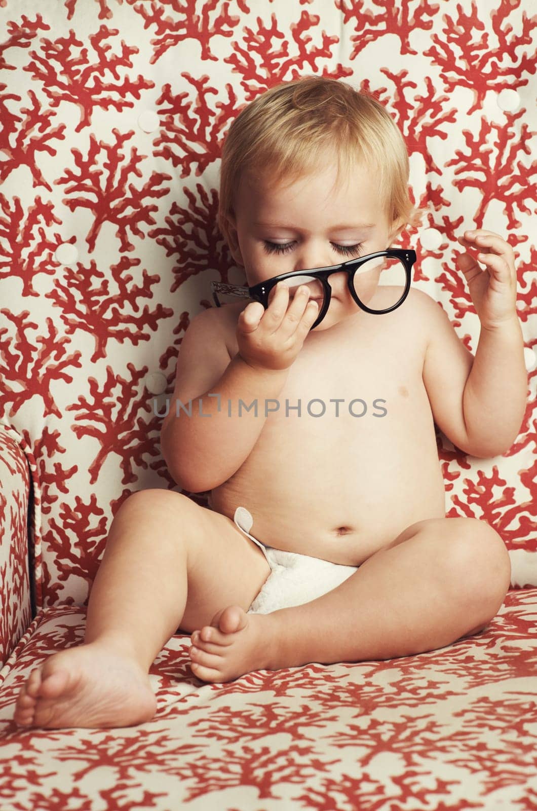 What a curious little guy. An adorable baby boy sitting in a nappy and playing with a pair of glasses. by YuriArcurs