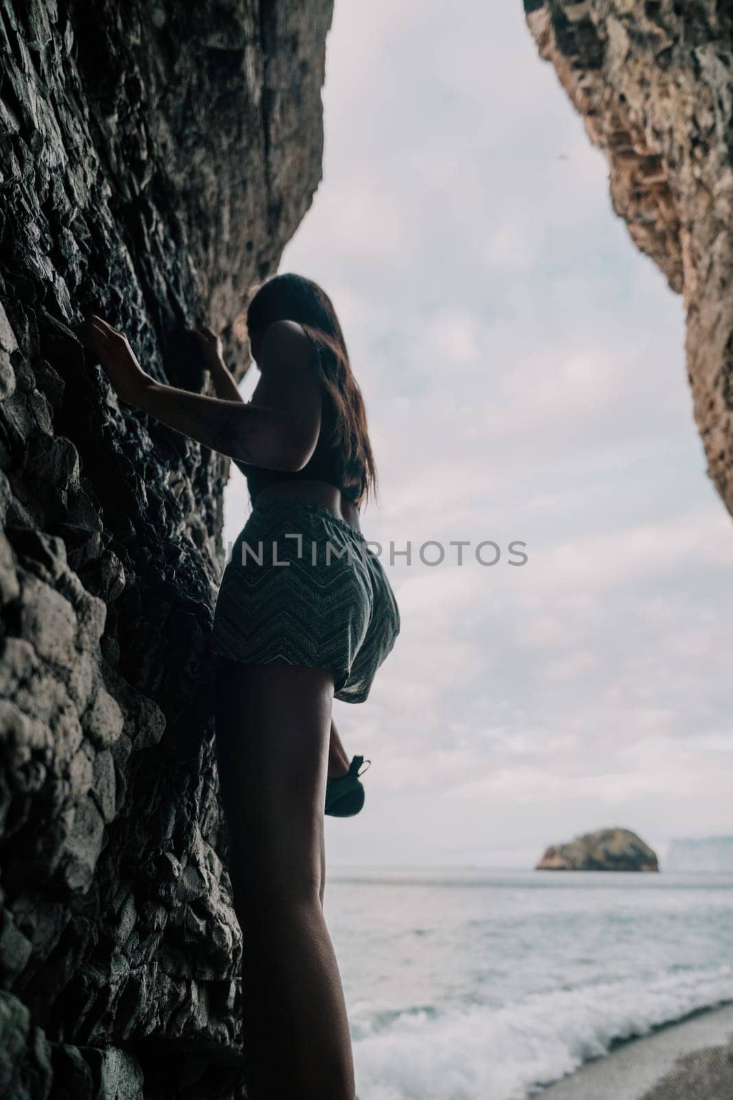 A girl climbs a rock. The athlete trains in nature. Woman overcomes difficult climbing route. Extreme hobby. Tourist woman rock climber hiking on mountains rocks over beautiful sea coast