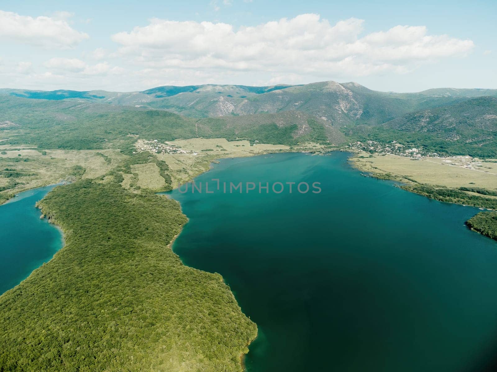 Aerial landscape from flying drone storage reservoir at mountain foot covered colorful spring forest. Beautiful view from above blue lake among highlands