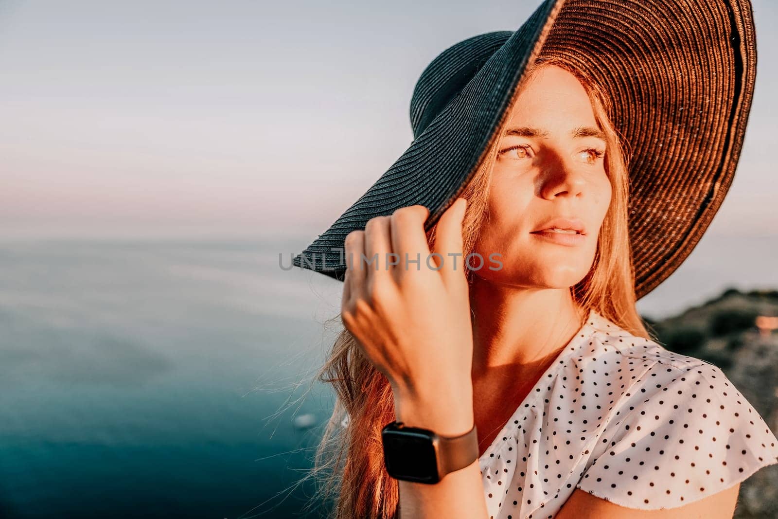 Portrait of happy young woman wearing summer black hat with large brim at beach on sunset. Closeup face of attractive girl with black straw hat. Happy young woman smiling and looking at camera at sea