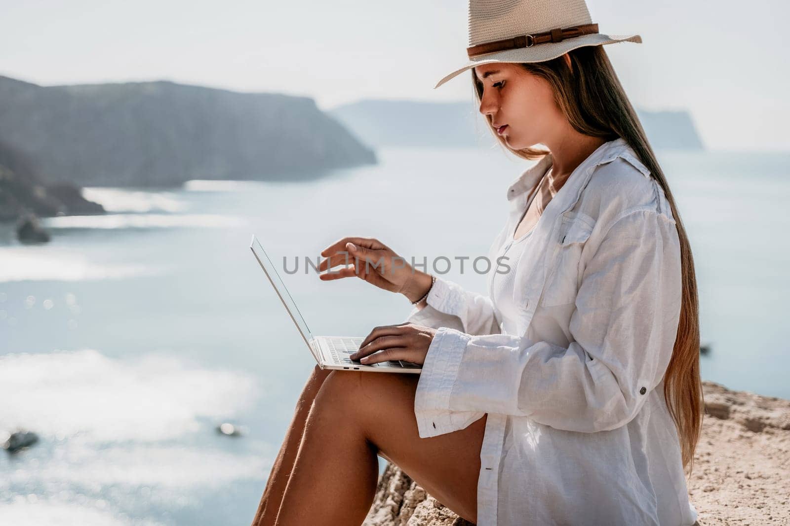 Woman sea laptop. Business woman in yellow hat freelancer with laptop working over blue sea beach. Girl relieves stress from work. Freelance, digital nomad, travel and holidays concept by panophotograph