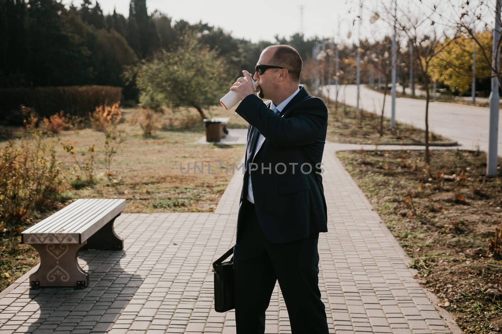 Mature entrepreneur drink coffee in autumn park. Senior executive rest in city park.