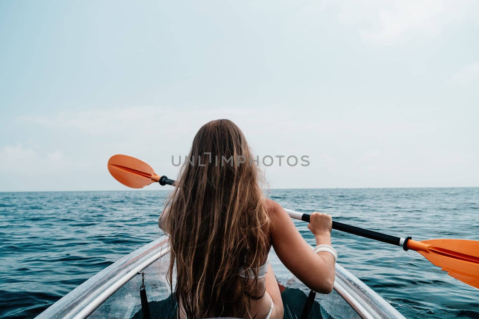 Woman in kayak back view. Happy young woman with long hair floating in transparent kayak on the crystal clear sea. Summer holiday vacation and cheerful female people having fun on the boat.