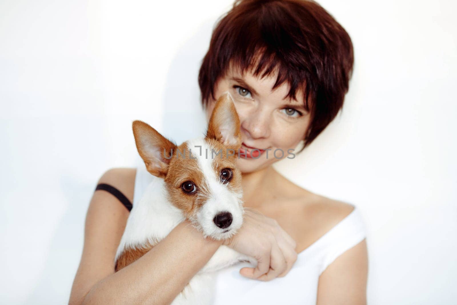 Portrait of good looking cheerful woman enjoys company of small pedigree dog wears white tank top spends free time with favorite pet isolated over white background. Animal owner