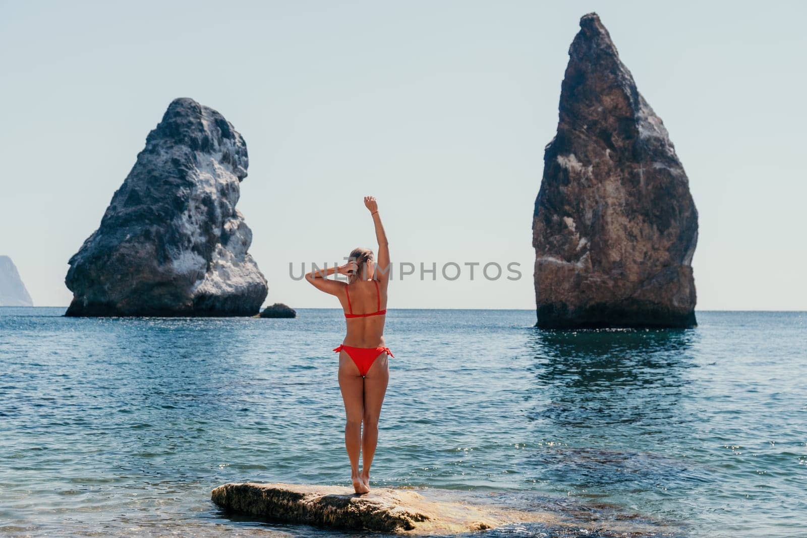 Woman travel sea. Young Happy woman in a long red dress posing on a beach near the sea on background of volcanic rocks, like in Iceland, sharing travel adventure journey