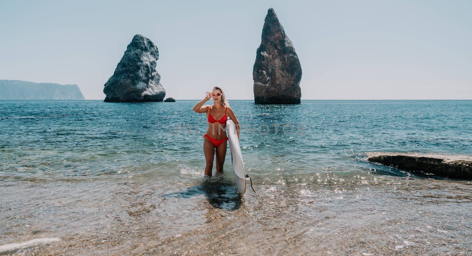 Close up shot of beautiful young caucasian woman with black hair and freckles looking at camera and smiling. Cute woman portrait in a pink bikini posing on a volcanic rock high above the sea
