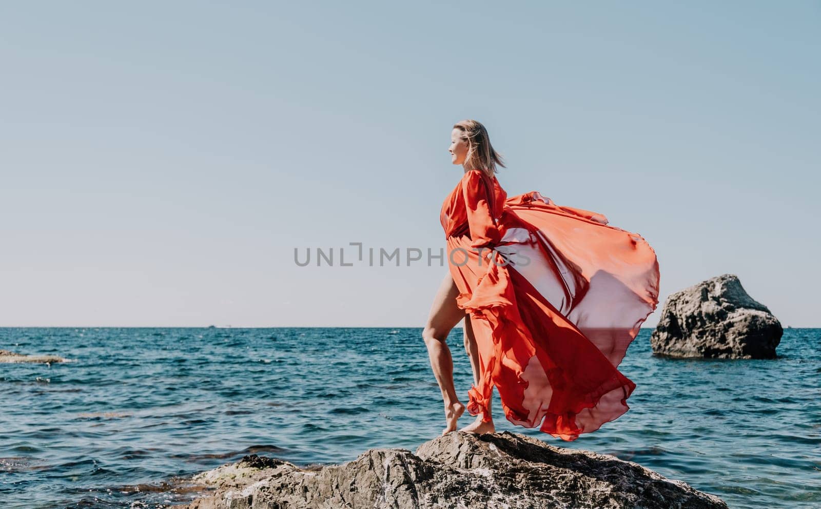 Woman travel sea. Young Happy woman in a long red dress posing on a beach near the sea on background of volcanic rocks, like in Iceland, sharing travel adventure journey