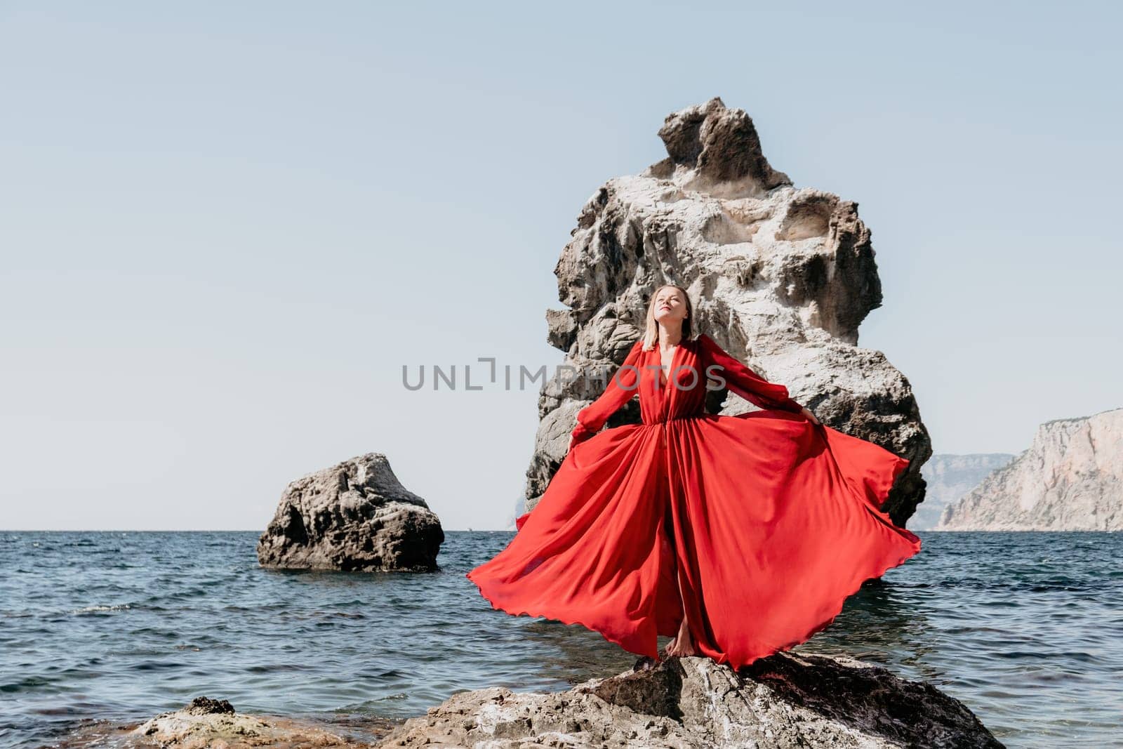 Woman travel sea. Young Happy woman in a long red dress posing on a beach near the sea on background of volcanic rocks, like in Iceland, sharing travel adventure journey