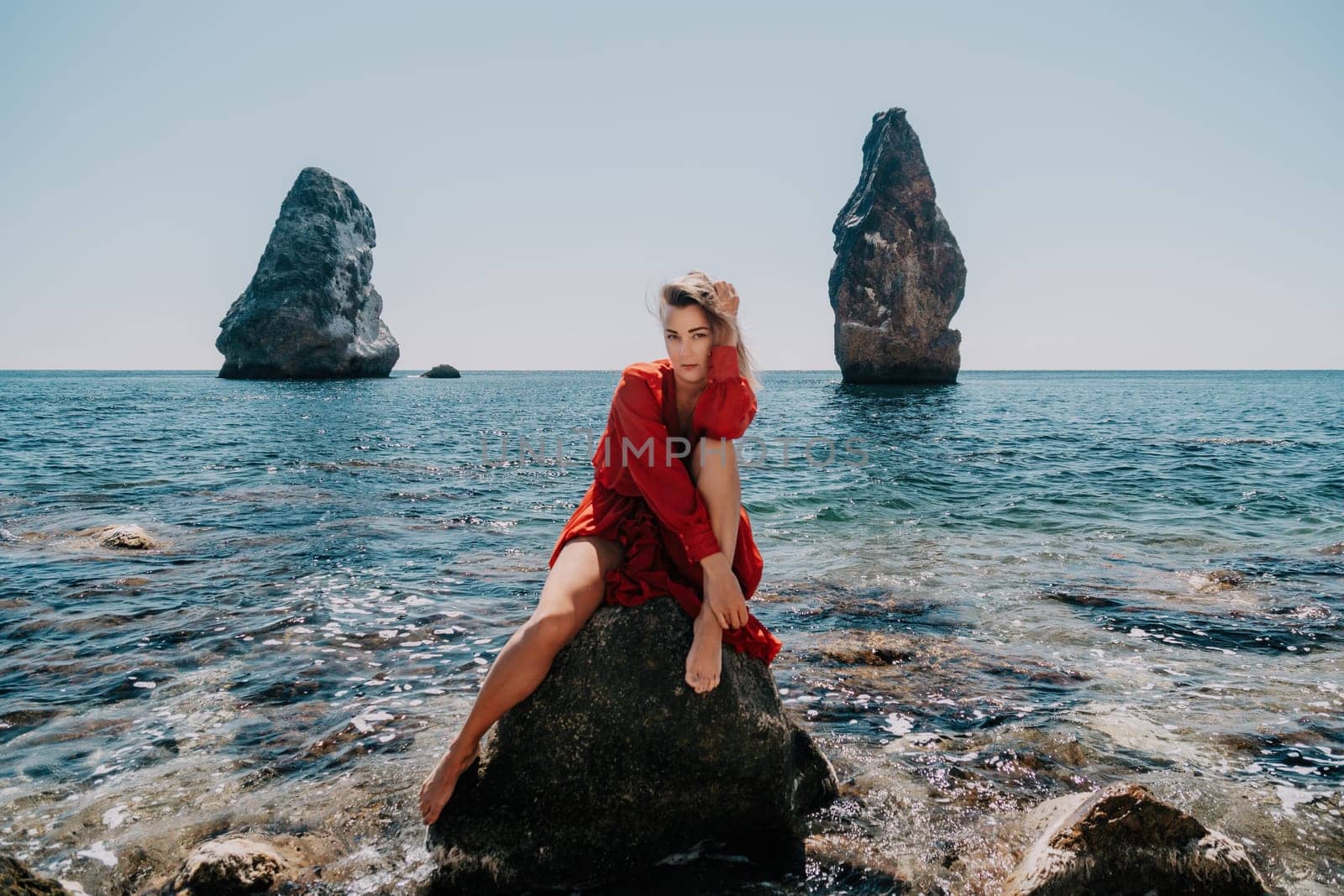 Woman travel sea. Young Happy woman in a long red dress posing on a beach near the sea on background of volcanic rocks, like in Iceland, sharing travel adventure journey