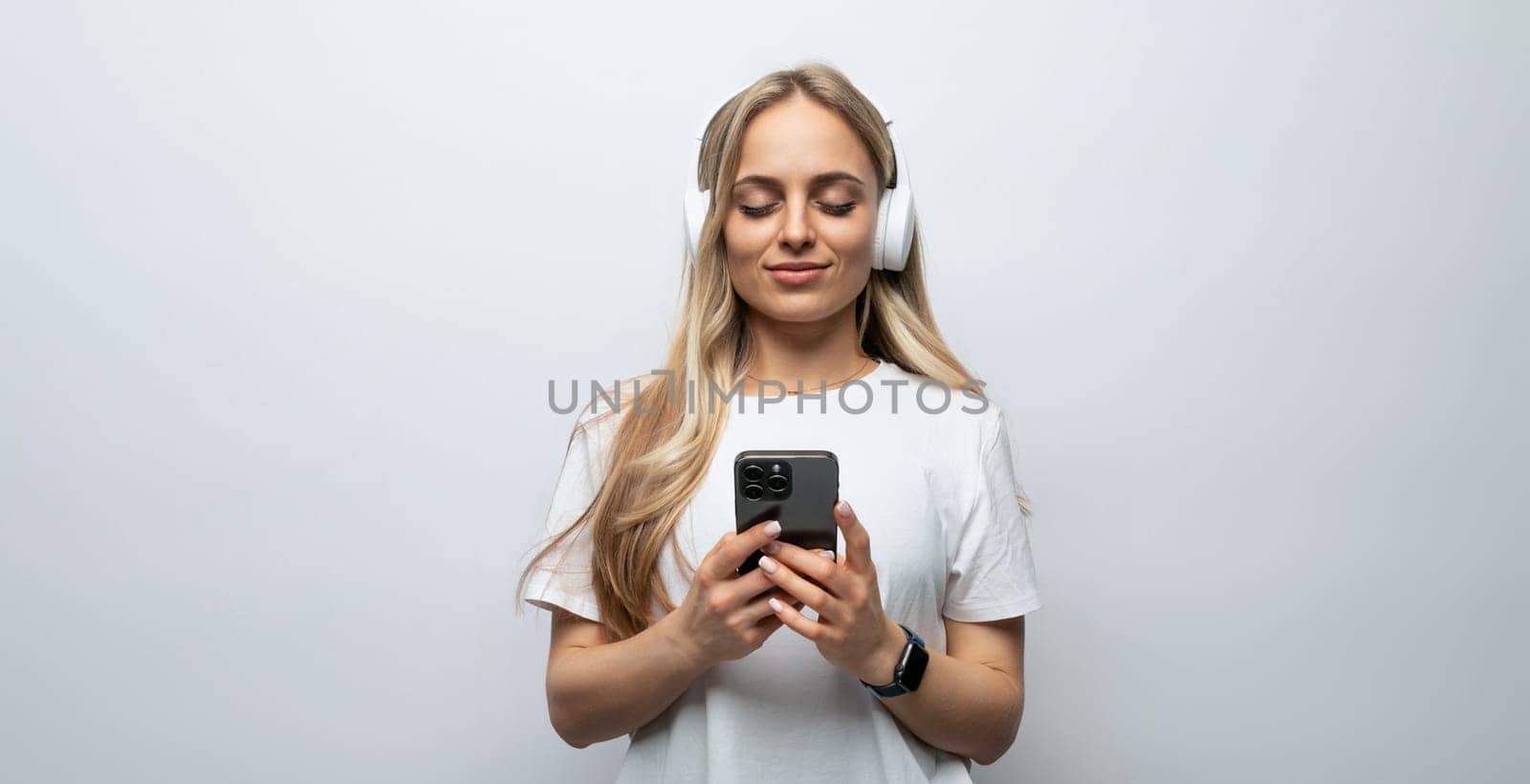 blogger girl with headphones on her head holding a phone in her hands on a white background.