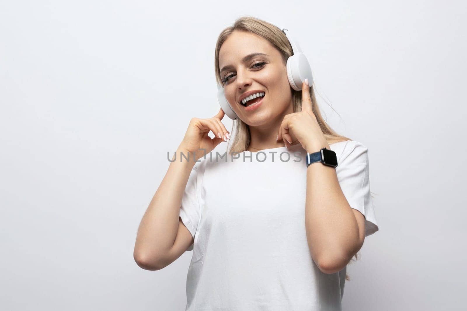 a girl in a white t-shirt listens to music in wireless headphones on a white background with empty space by TRMK